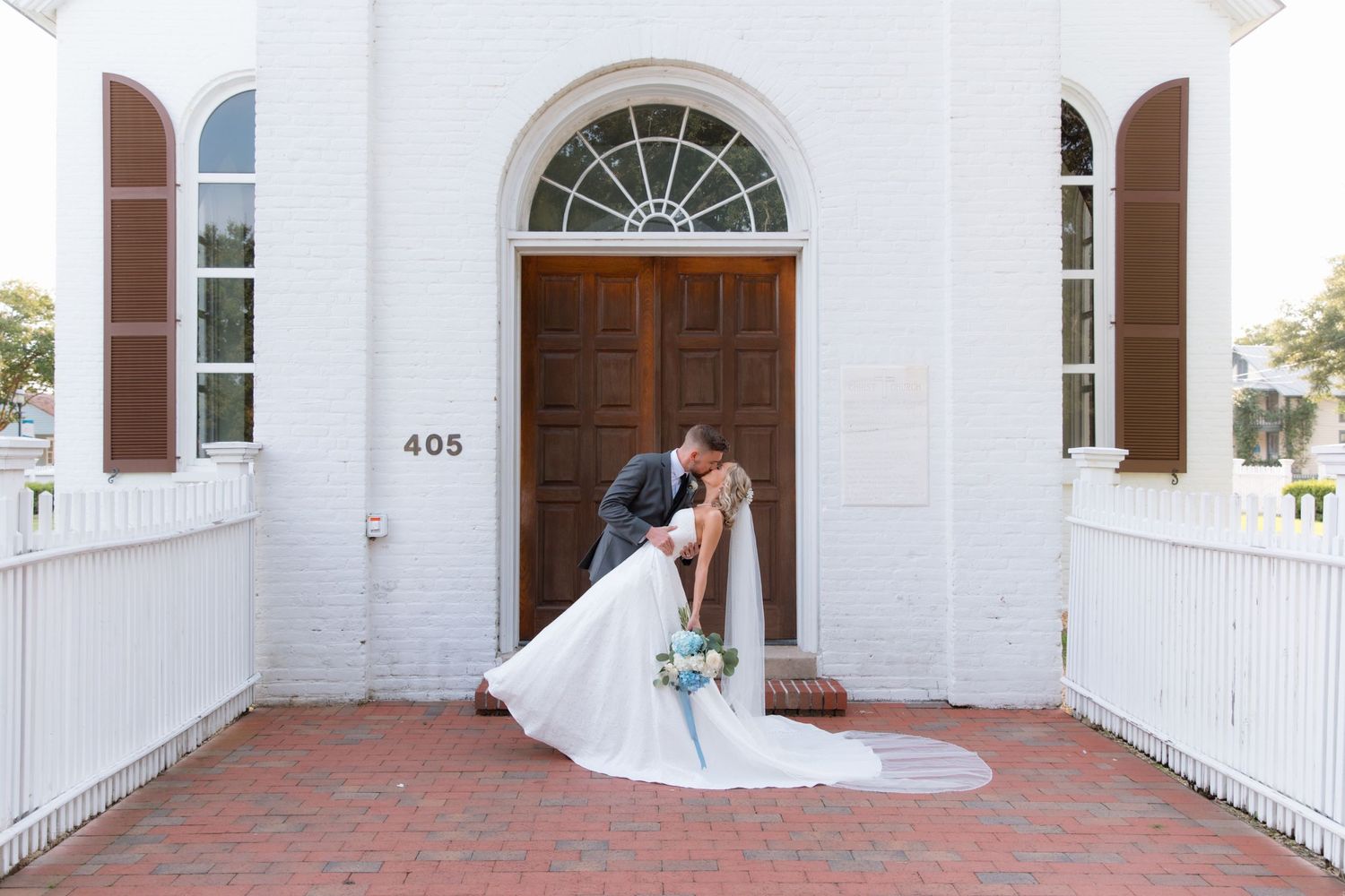 Wedding couple shares romantic kiss in front of classic white church entrance with address 405.