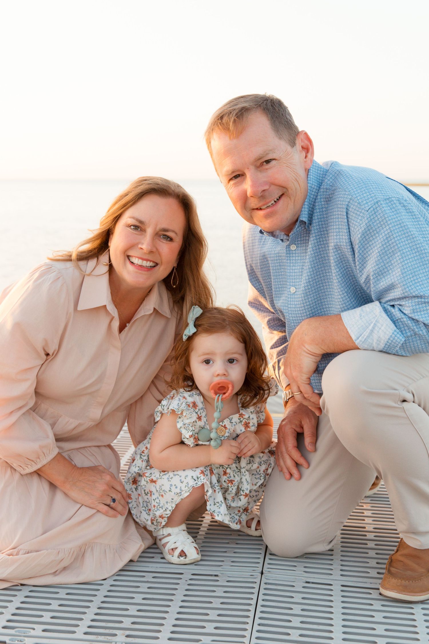 Family poses playfully on a wooden deck during sunset photoshoot in coordinating blue and beige outfits.