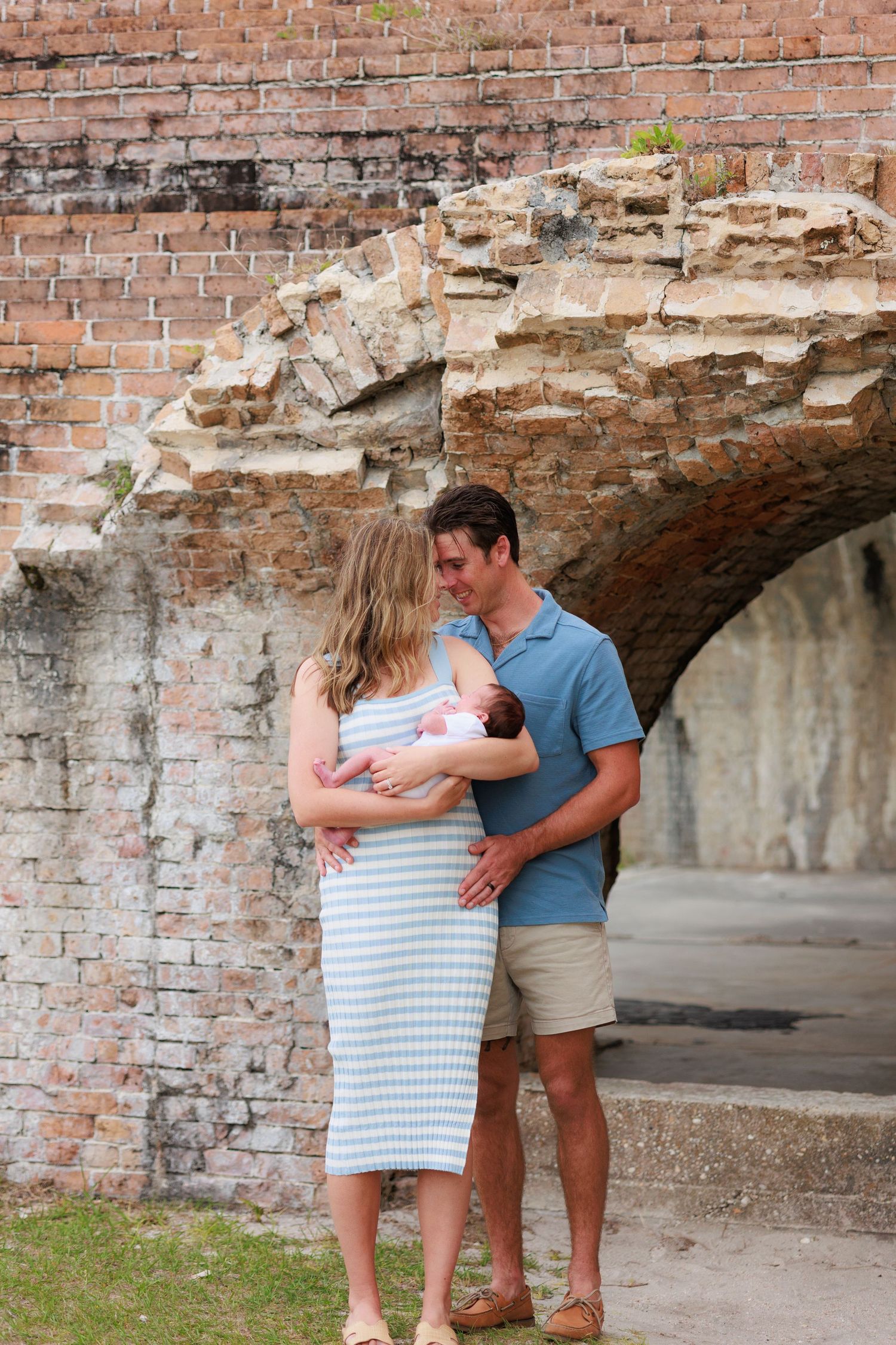 A couple embraces while standing in front of a rustic brick archway during a romantic outdoor photoshoot.