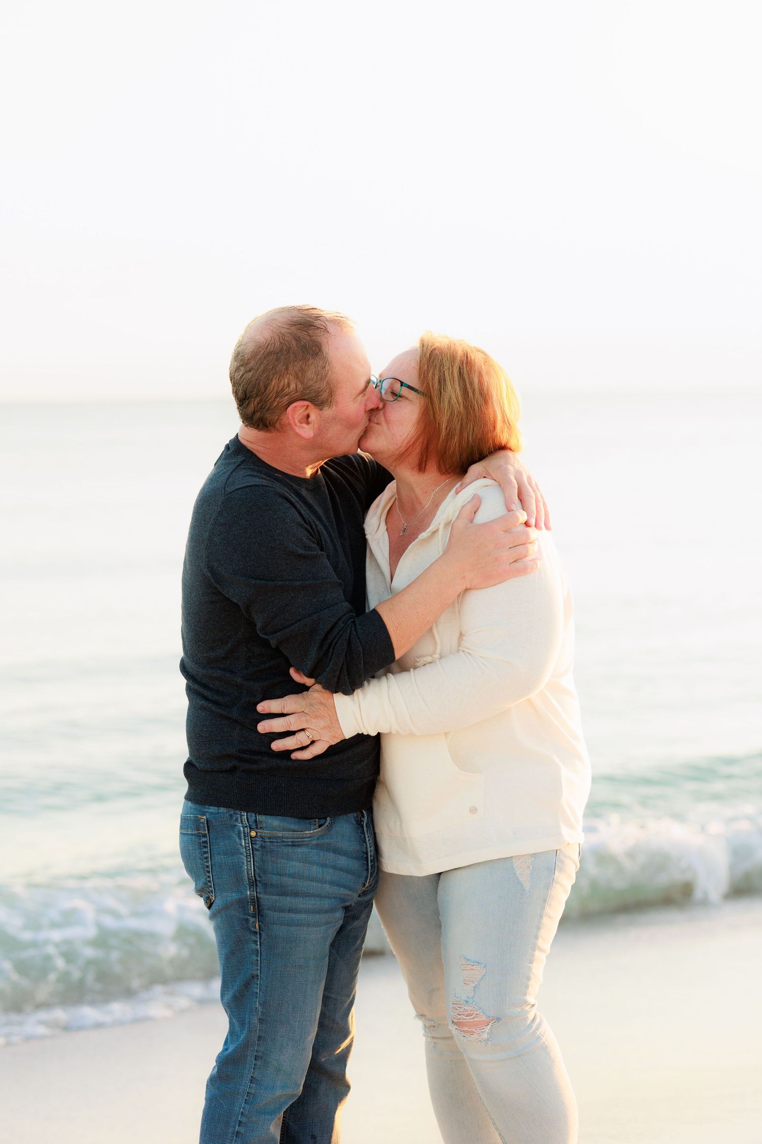 A romantic couple shares tender moments and kisses on a sunny beach with waves in the background.