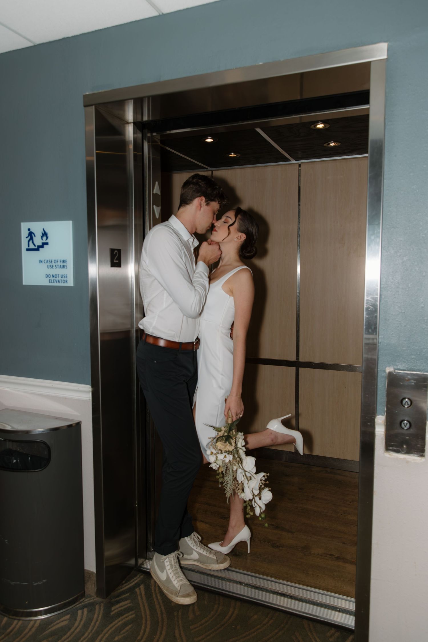 A couple shares a romantic moment in front of an elevator during their wedding celebration.