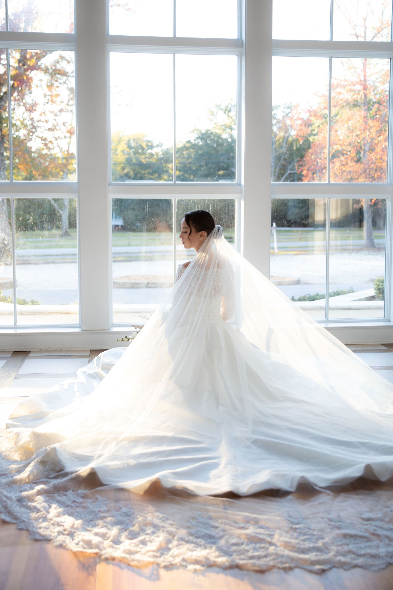 Dramatic bridal gown spread across a bright room with large windows and autumn views.