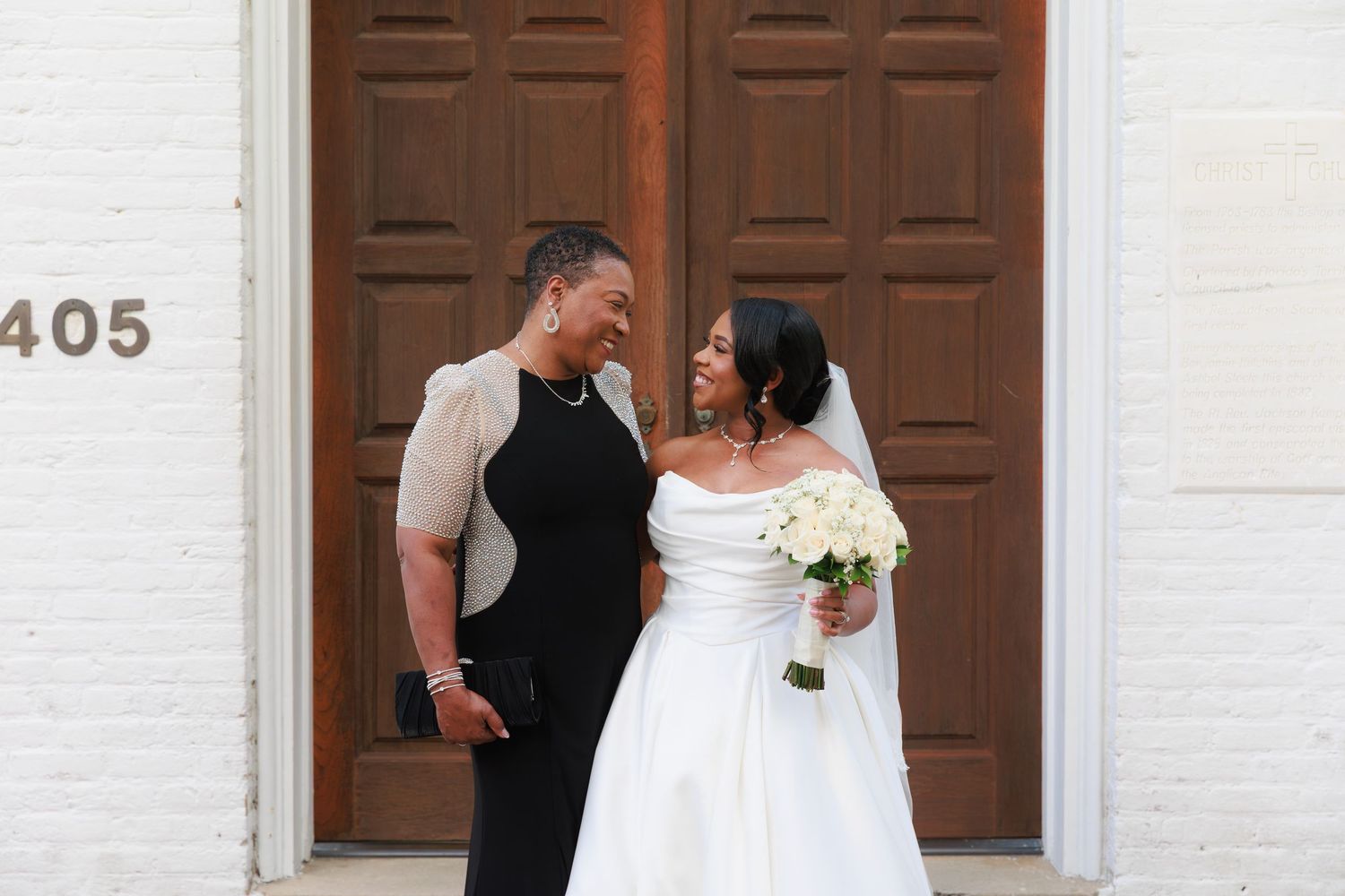 Wedding party members share a candid moment on red brick steps outside a white church building.
