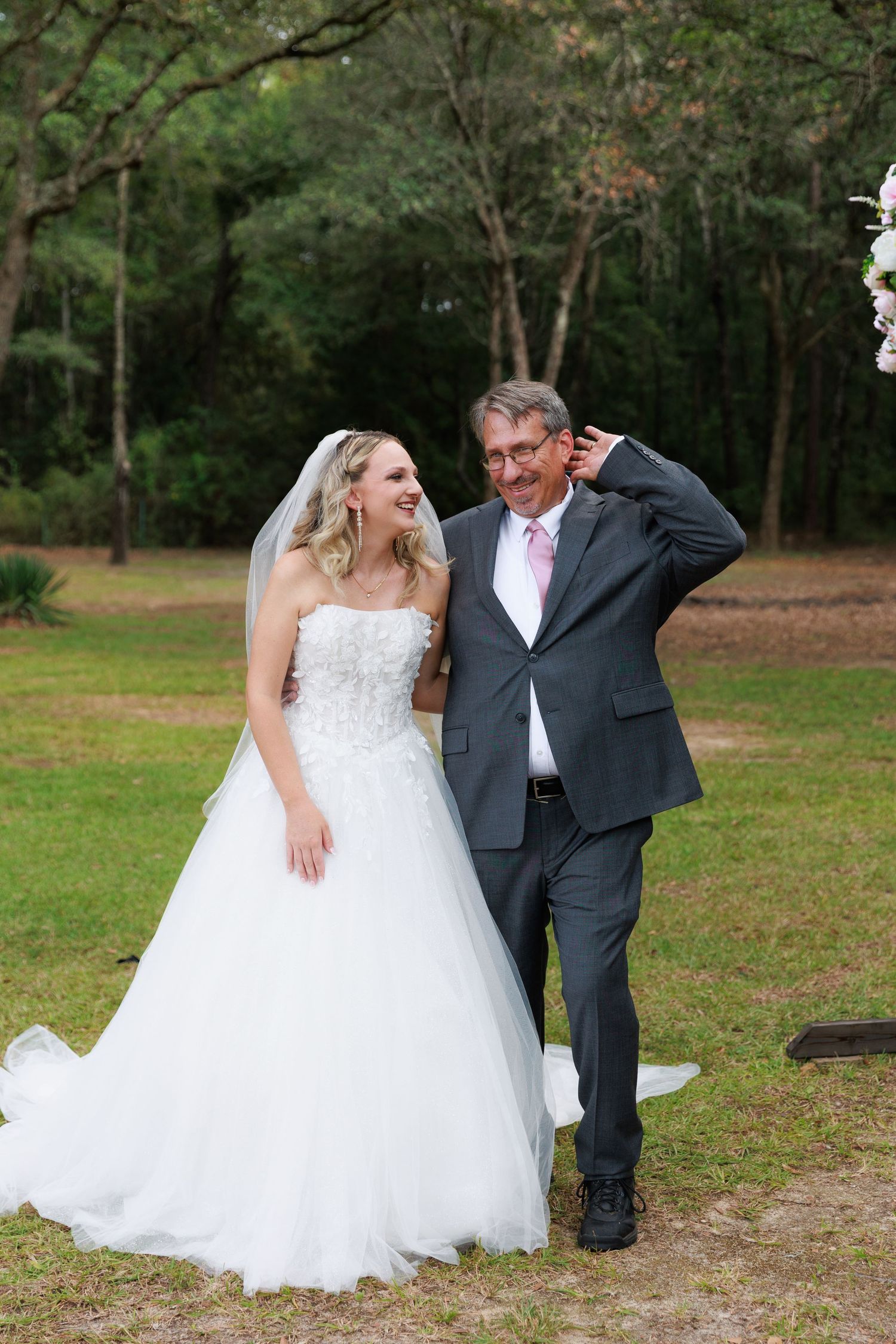 A joyful wedding moment captured outdoors with a bride in a white ballgown and companion in a gray suit.