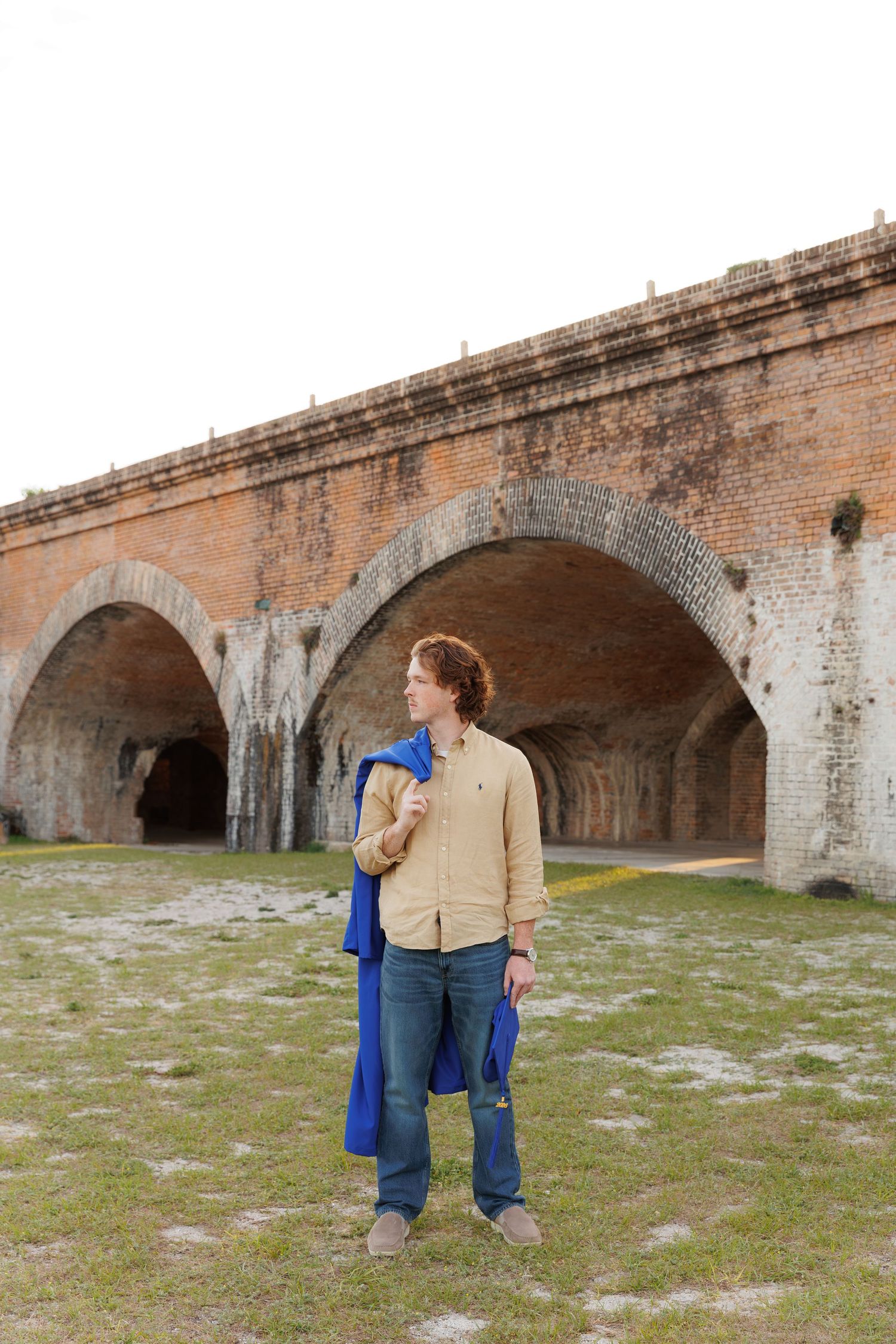 Young man with red hair holding a blue jacket stands before historic brick arches at Fort Jefferson, Dry Tortugas.
