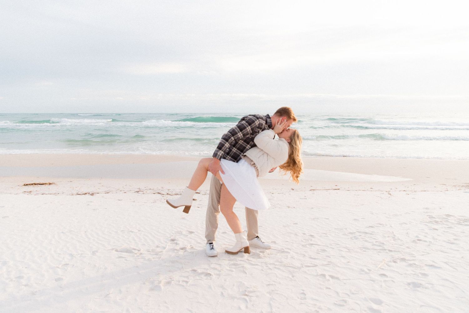 Couple enjoying a romantic moment together on a sunny white sand beach at sunset.