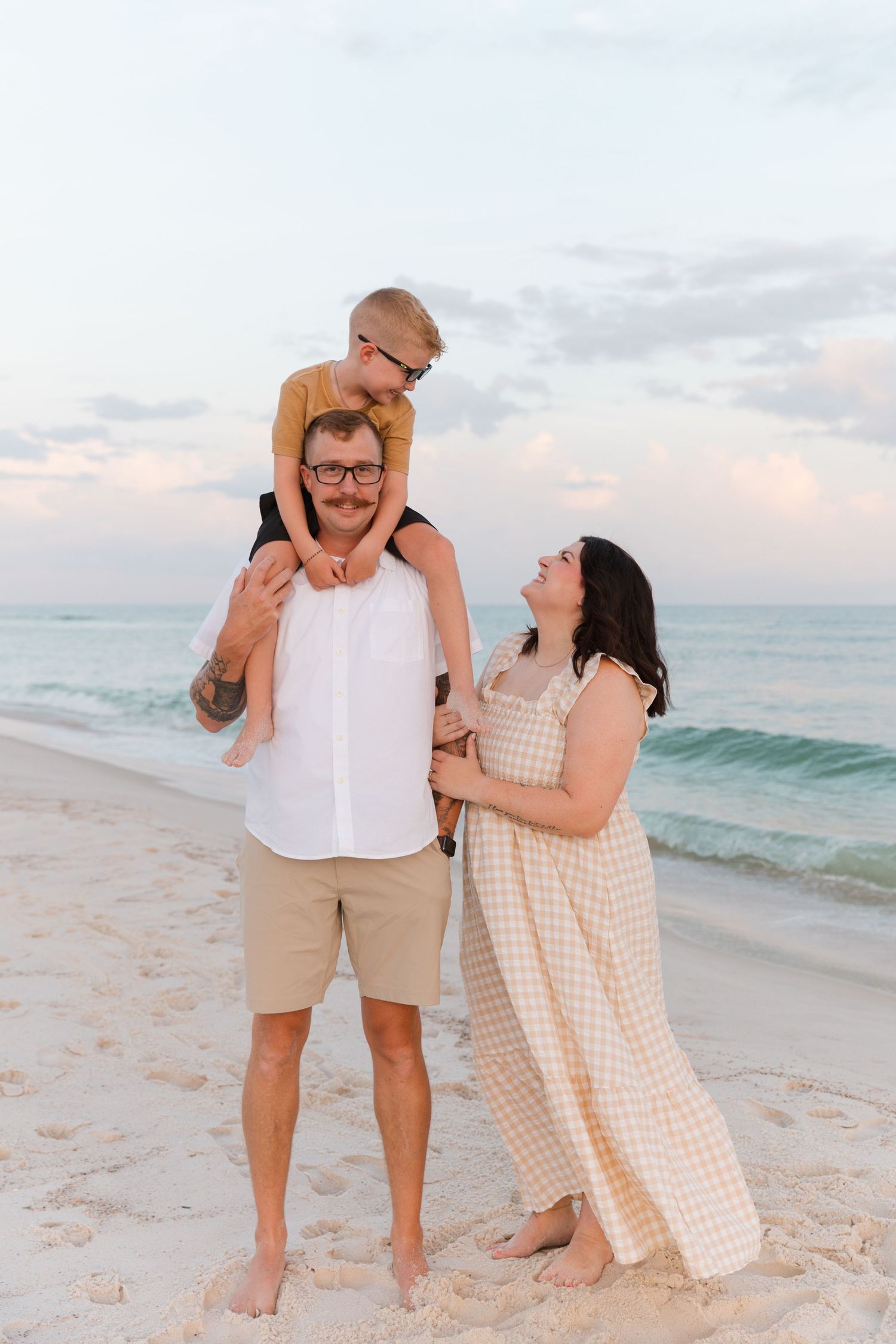 A family shares a joyful moment together on a sandy beach at sunset with ocean waves in the background.