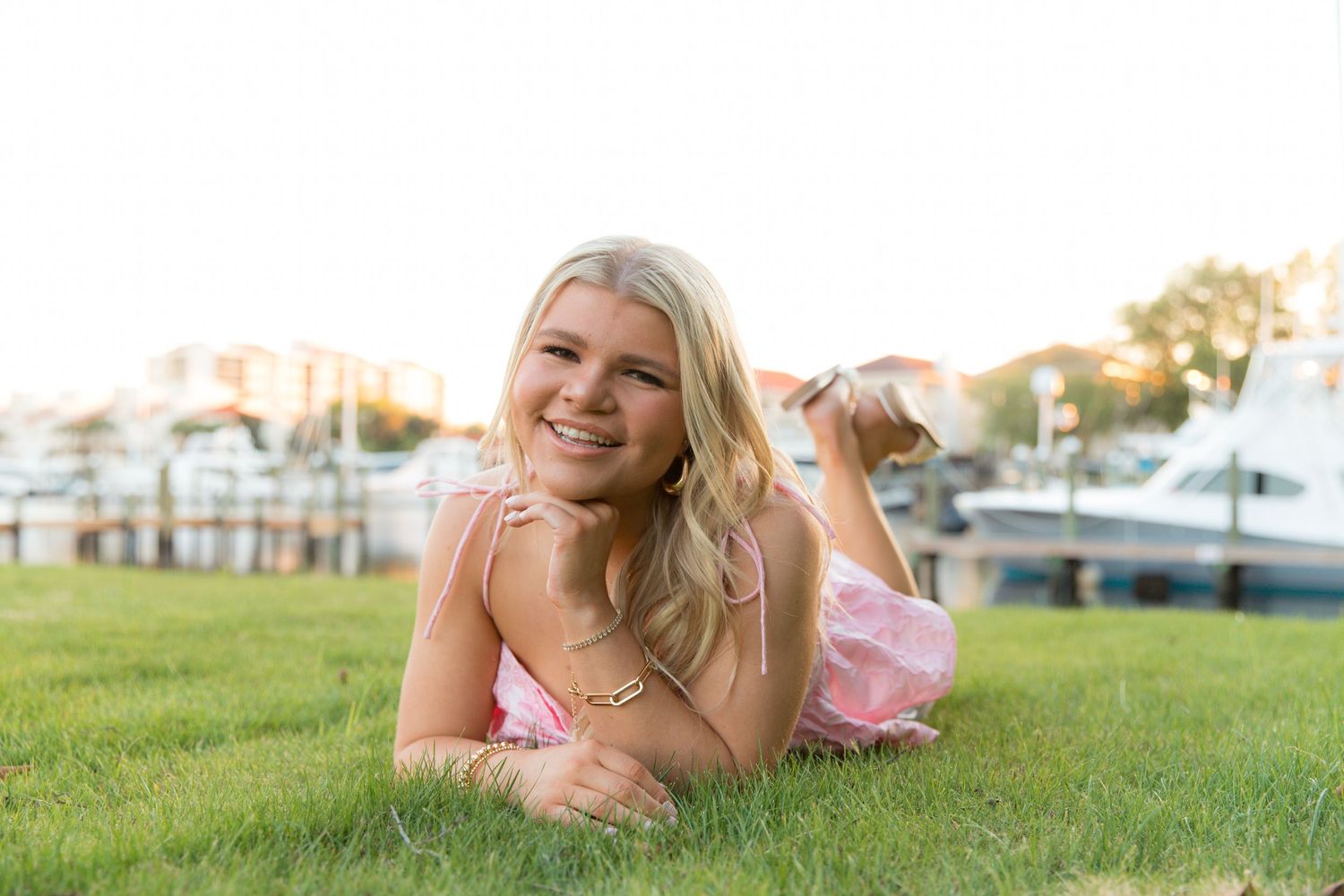 A person lies on lush green grass while smiling at the camera during a sunny outdoor photoshoot.