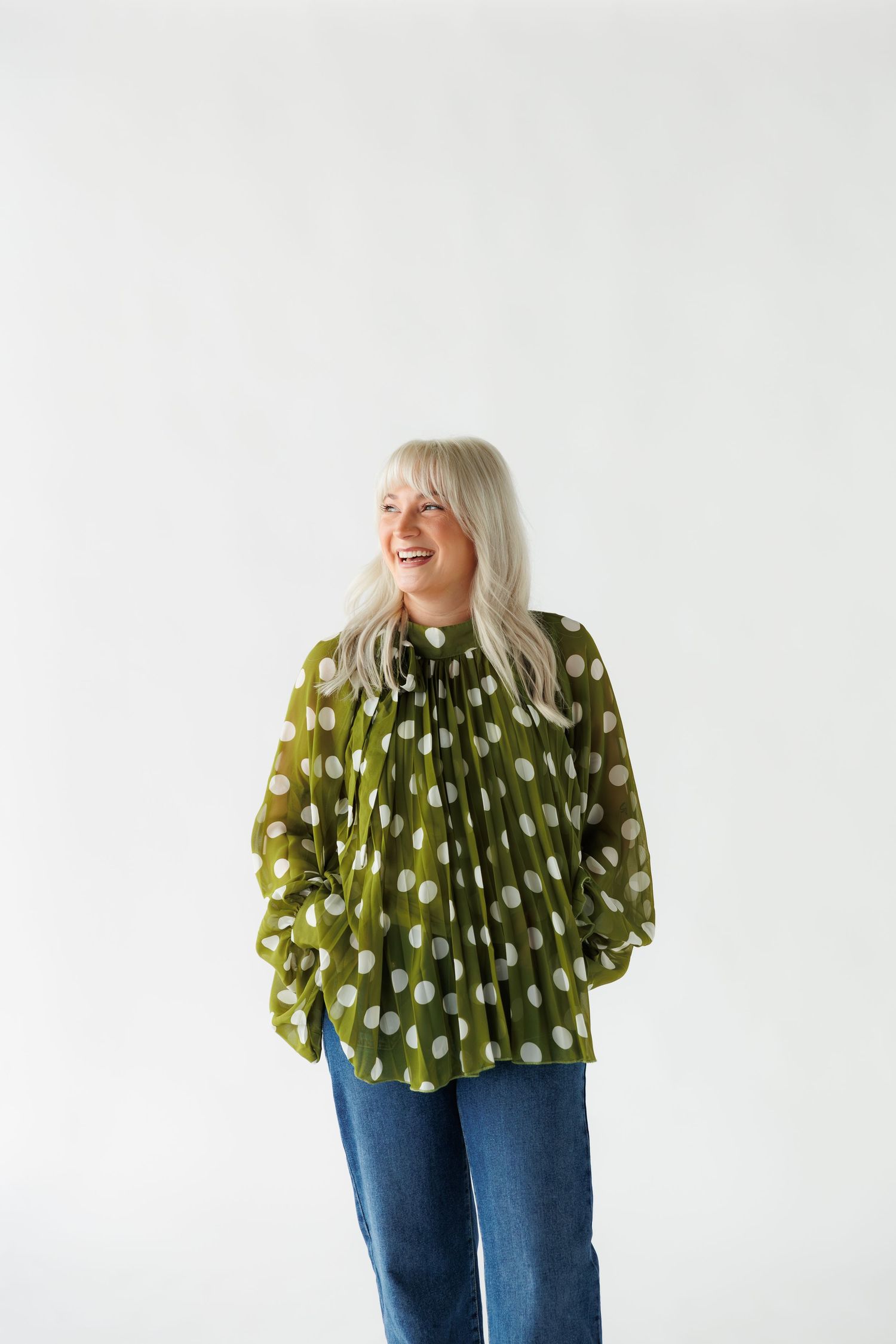 A person wearing a polka dot green blouse and blue jeans poses in a sequence of five playful expressions.