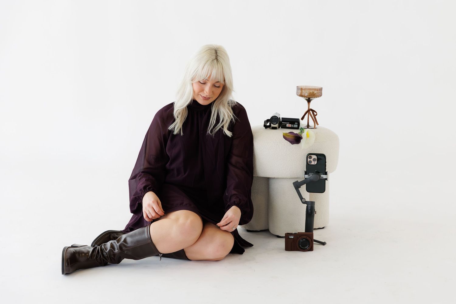 A person in a black sweater poses on a white floor in a minimalist studio setting.
