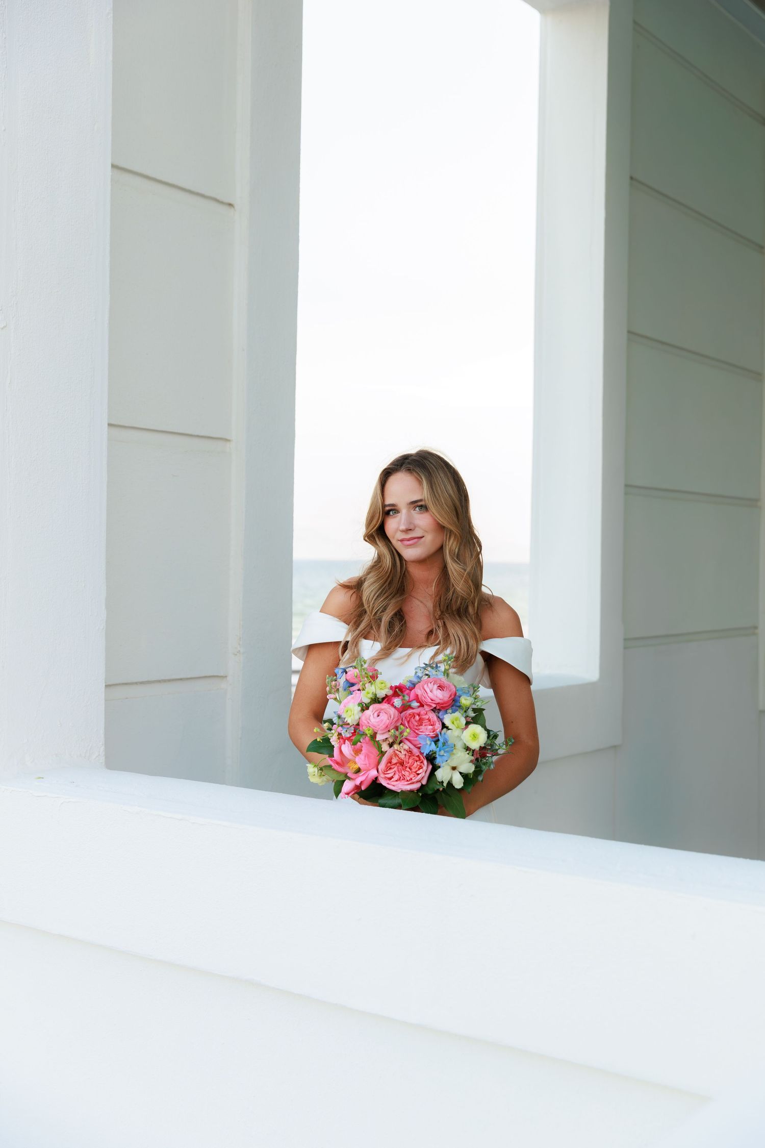 Beautiful bridal portrait in white architectural setting with colorful floral bouquet.