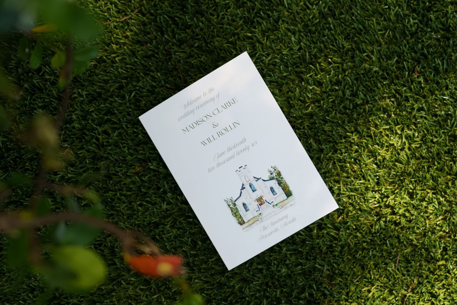 Wedding program booklet with illustrated church design laying on lush green grass lawn.