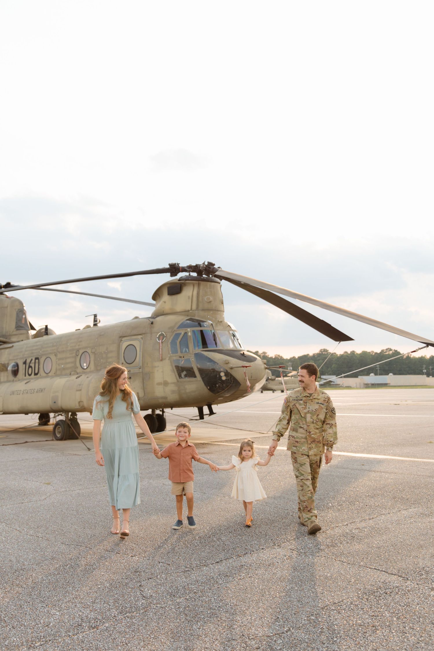Family walking together on airfield with military helicopter in background.