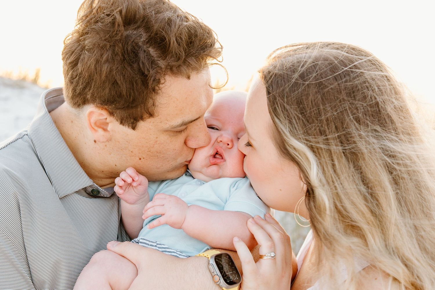 Parents sharing tender moment with baby between them during outdoor photoshoot.