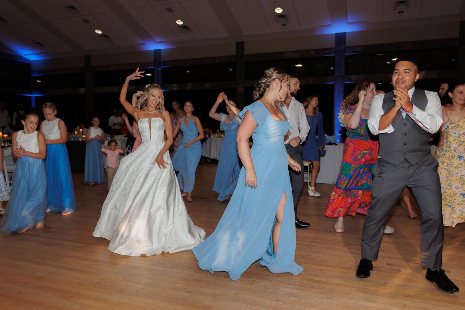 Wedding party dancing together on a wooden floor with blue bridesmaids dresses.