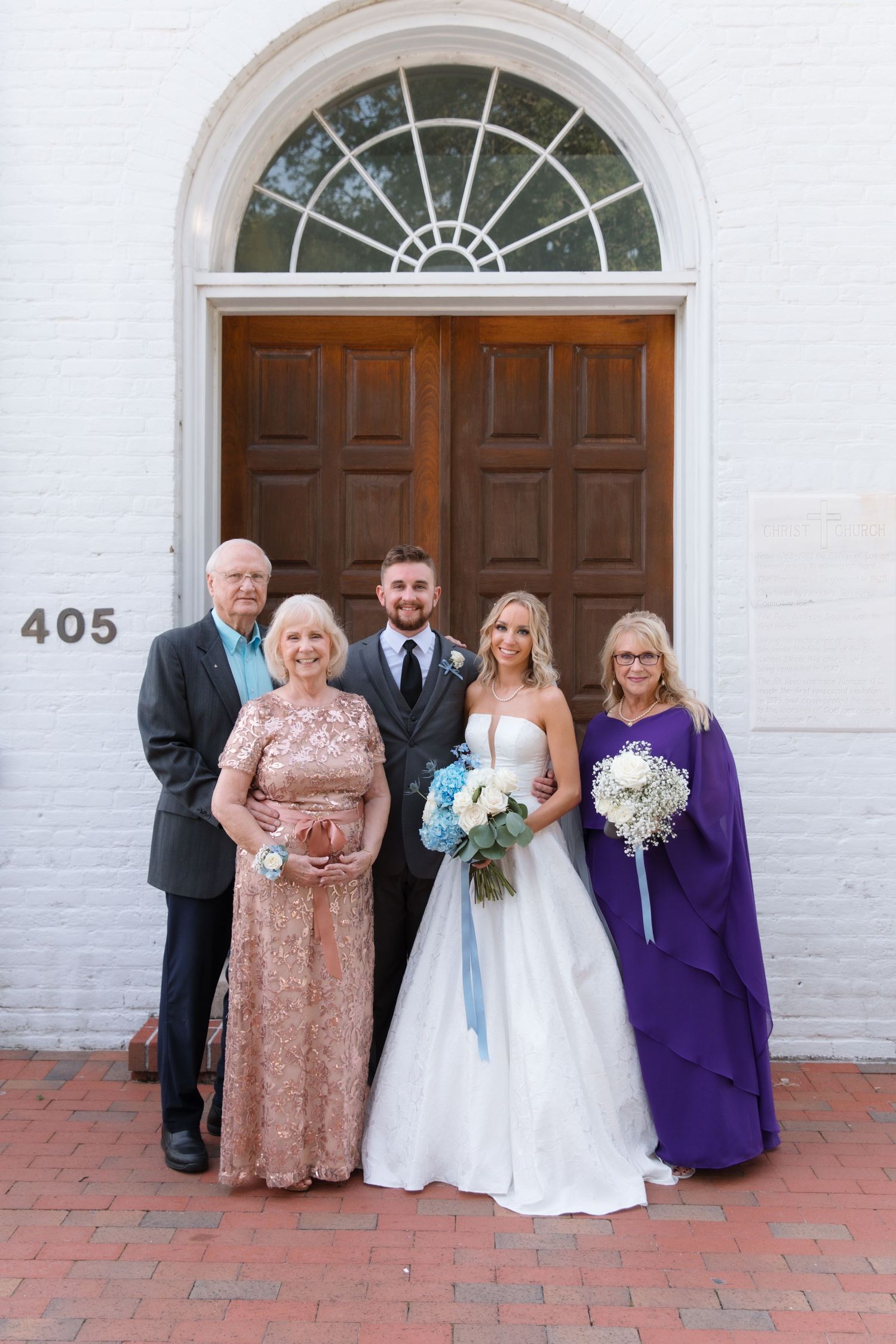 Family group portrait in formal attire standing in front of classic white church entrance.