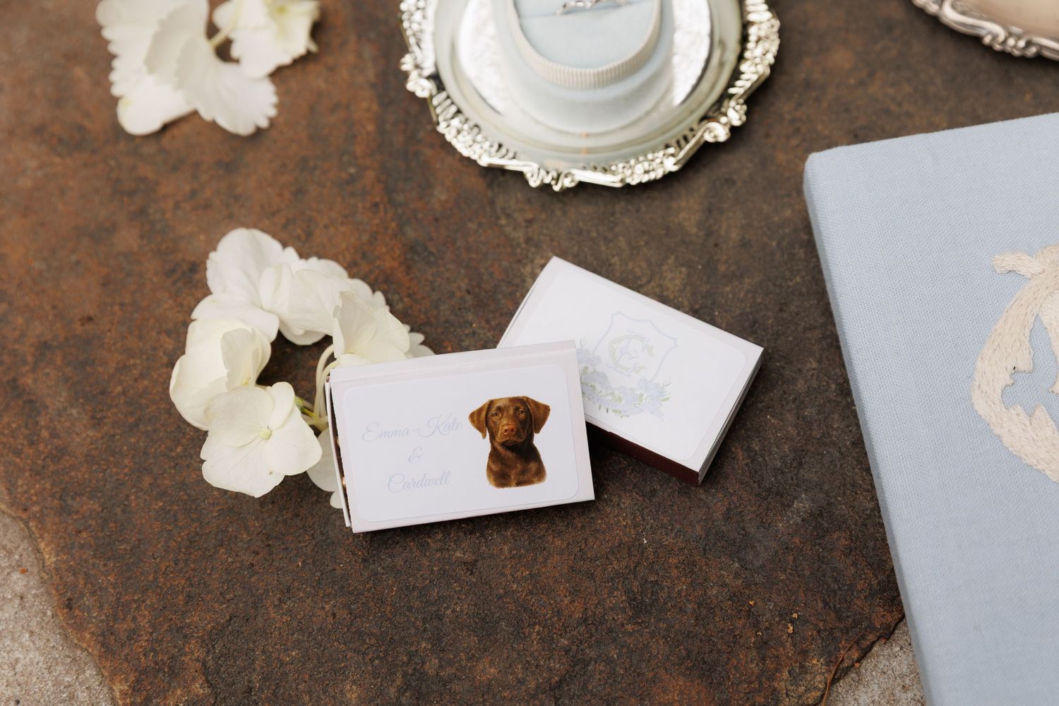 Custom wedding favor boxes with brown dog portrait design displayed on rustic surface with white flowers and silver tray.