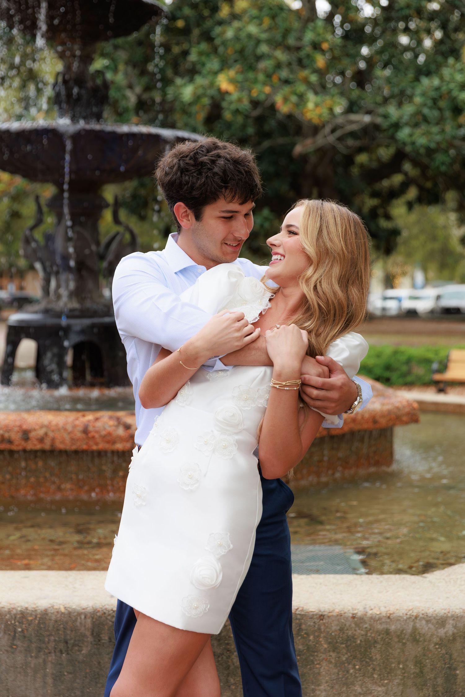 A joyful couple laughs together while embracing near a decorative water fountain.