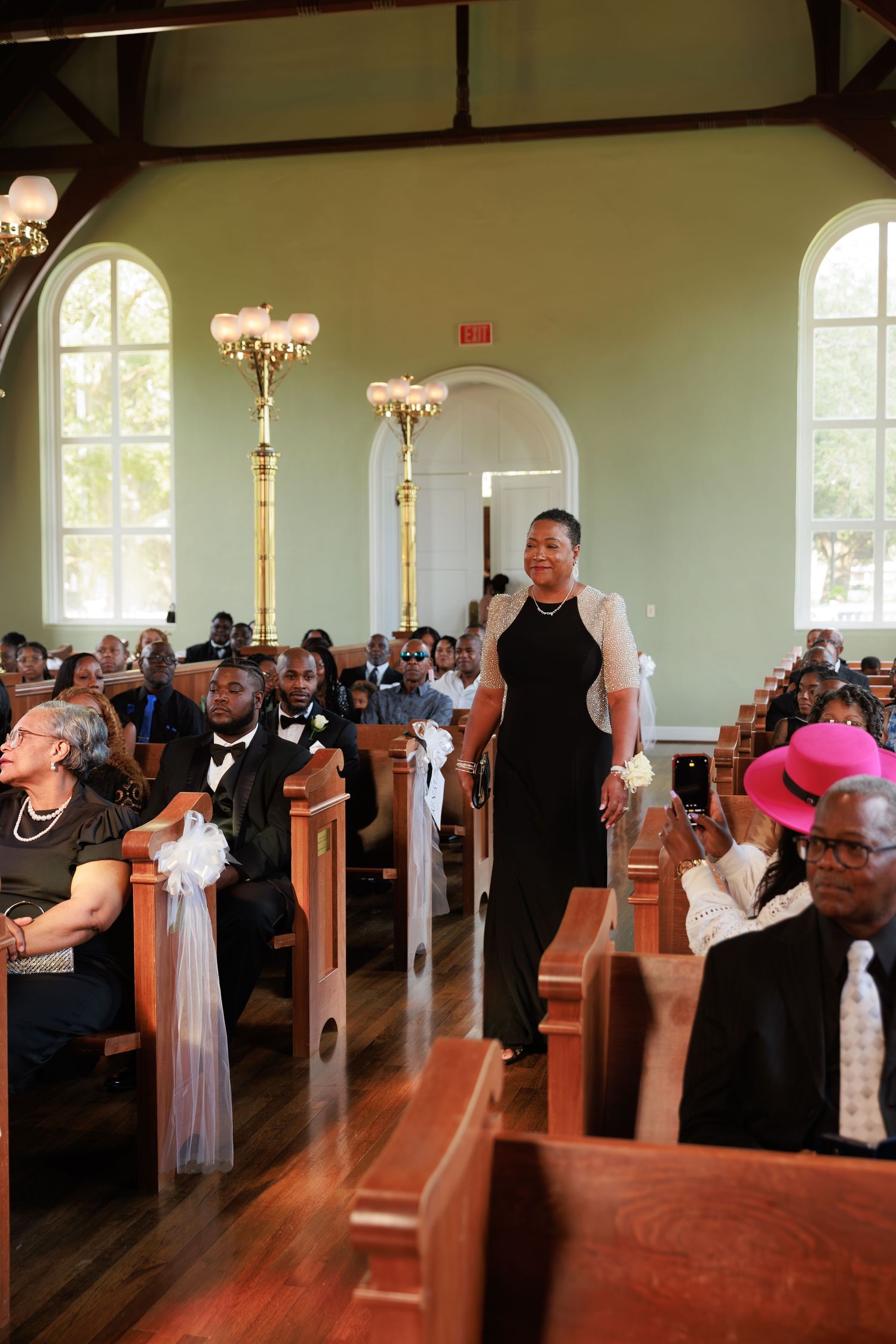 Wedding guests seated in wooden church pews decorated with white bows and pink accents.