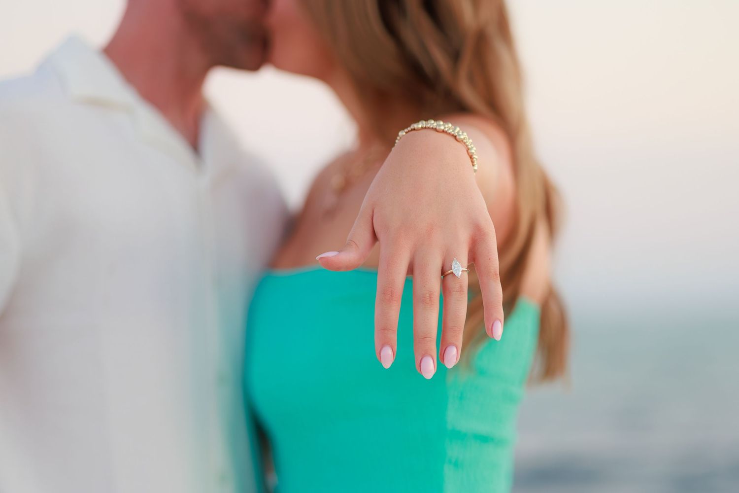 Close up of an engagement ring being shown on a hand wearing a turquoise colored top.
