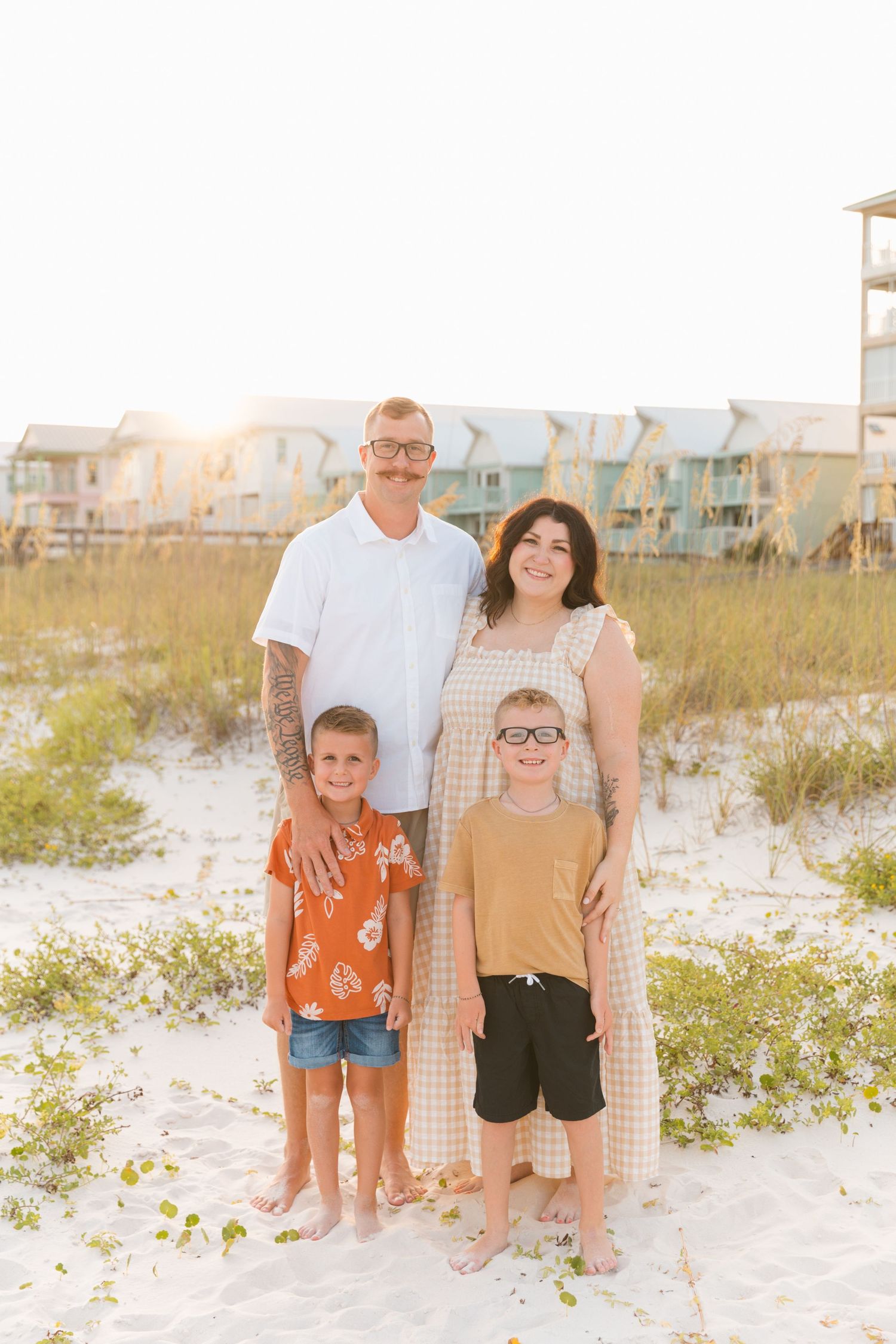 Family portrait session at sunset on a white sand beach with coastal homes in the background.
