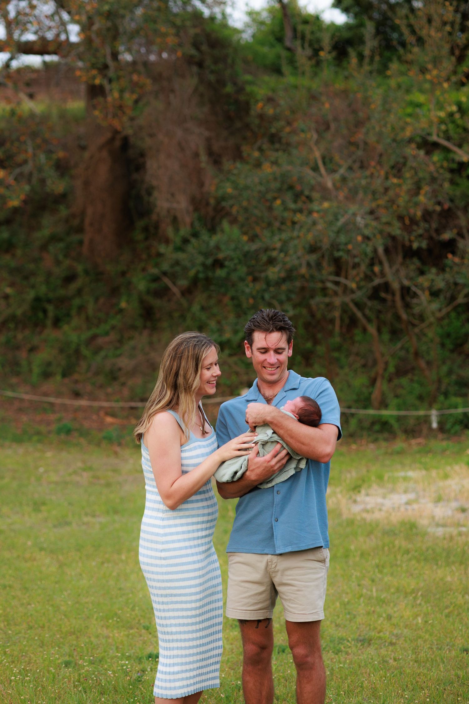 A family shares joyful moments together outdoors while holding their newborn baby.