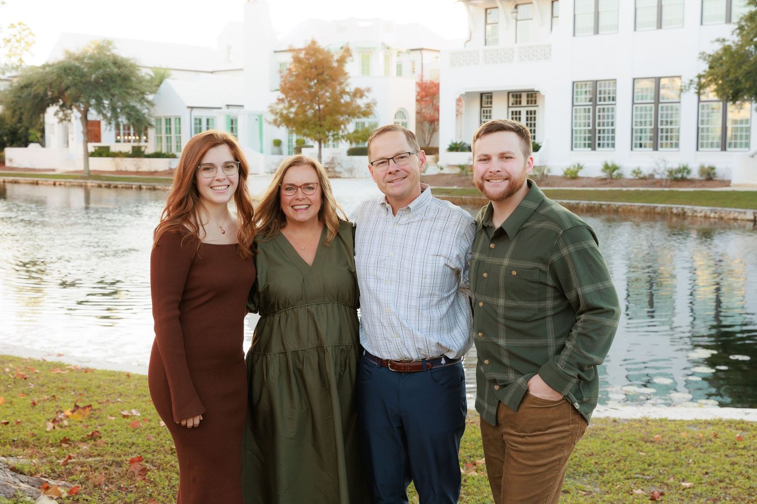Family group portrait of four people standing together by a waterfront with buildings in background.
