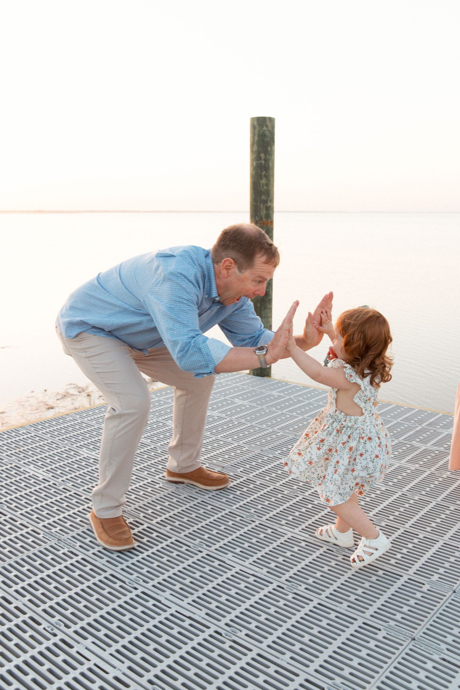 Parent and child playing together on a wooden pier by the ocean at dusk.