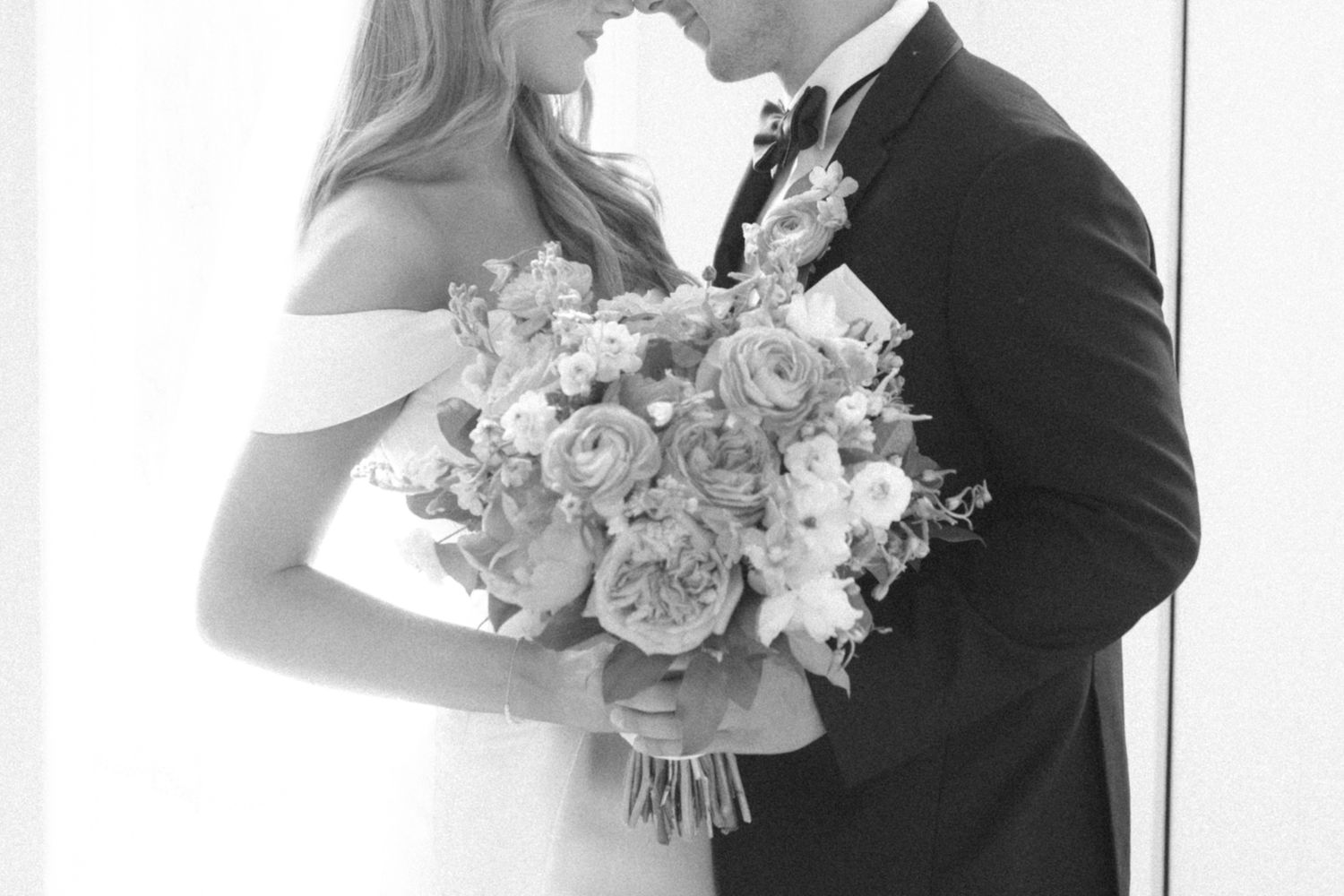A couple shares an intimate kiss at their wedding ceremony while holding a white floral bouquet.