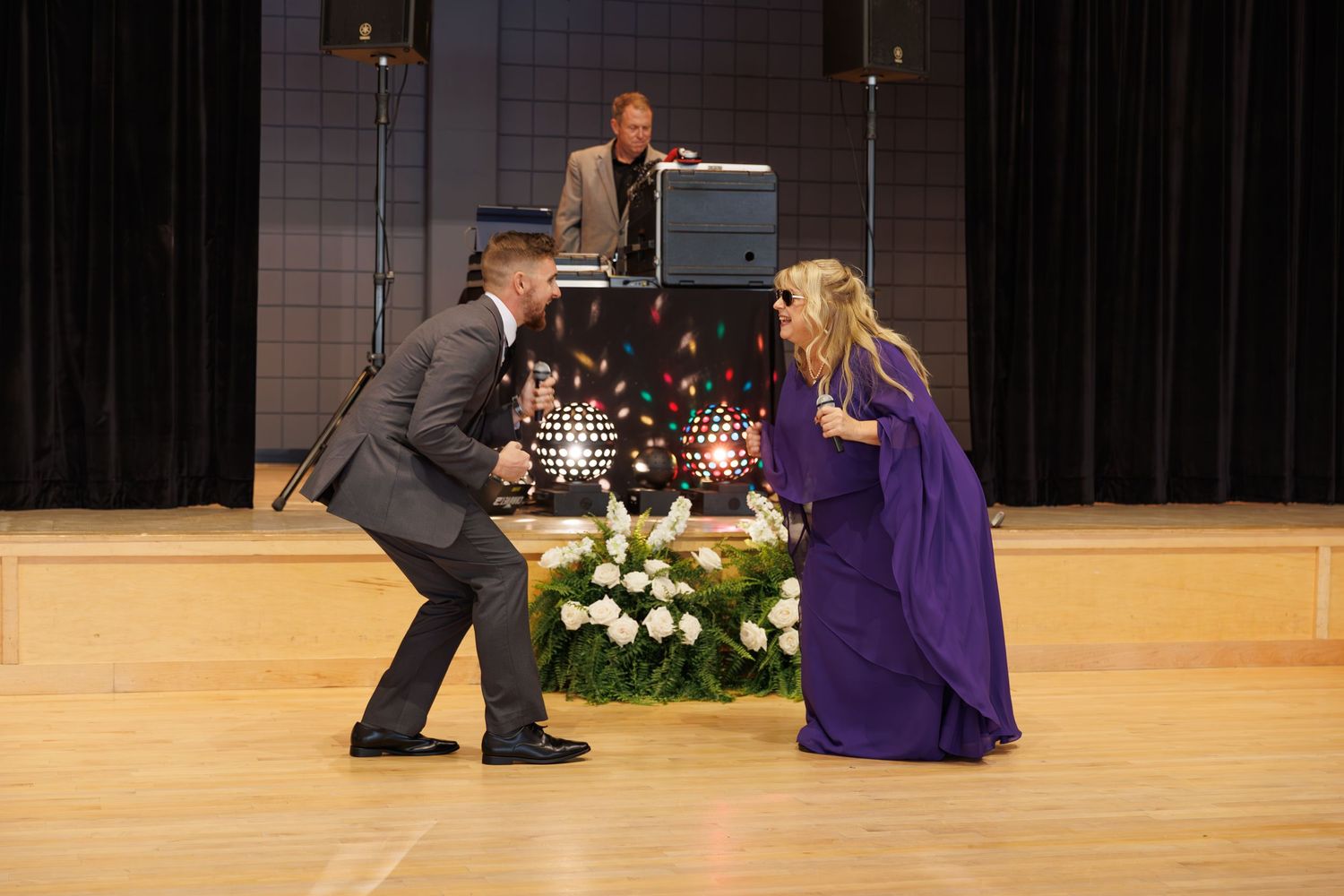 Two performers in grey suit and purple dress dance dramatically on a wooden stage.