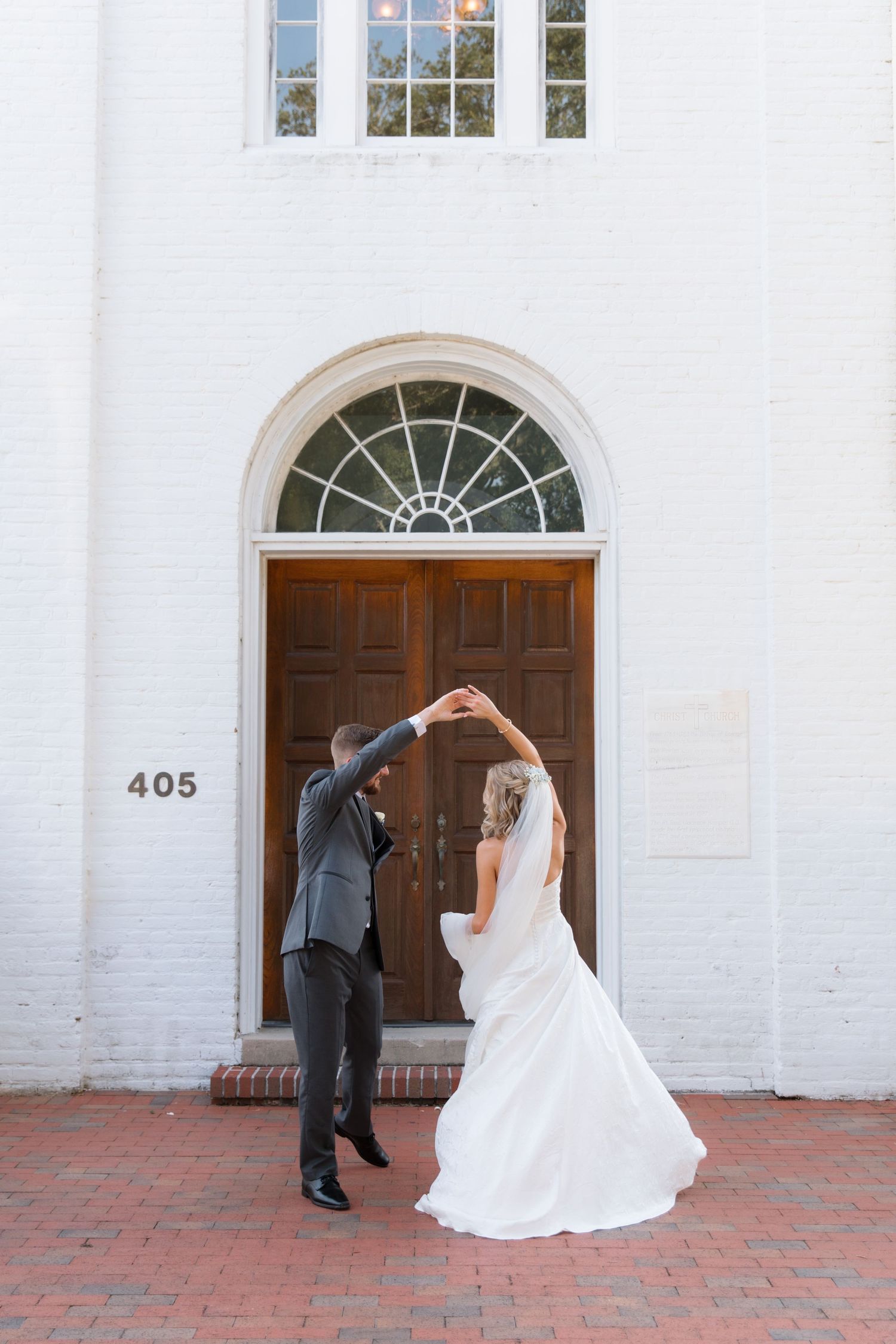 Wedding couple forms heart shape with arms in front of church entrance.