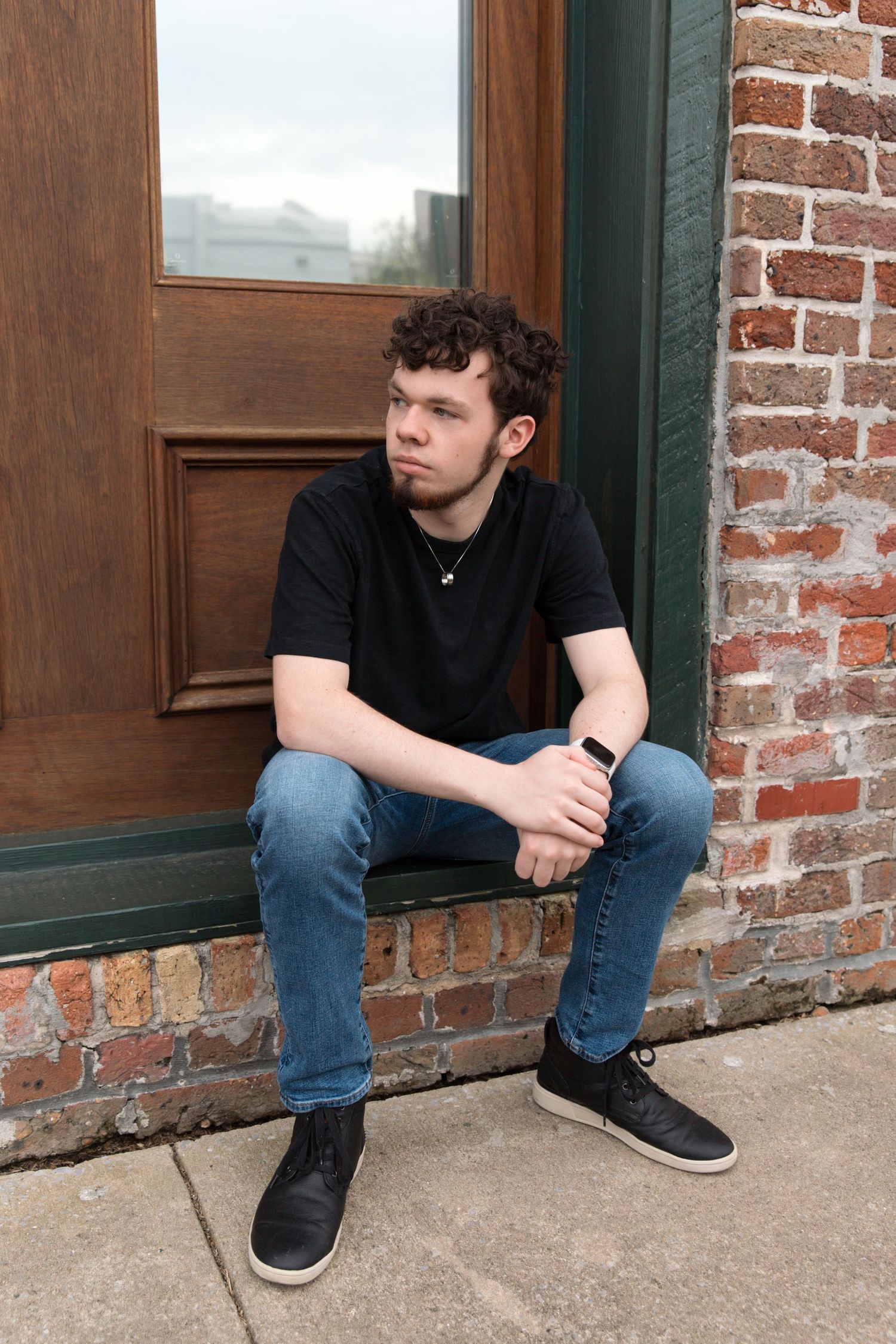 Person in black shirt sitting on brick windowsill wearing jeans and sneakers.