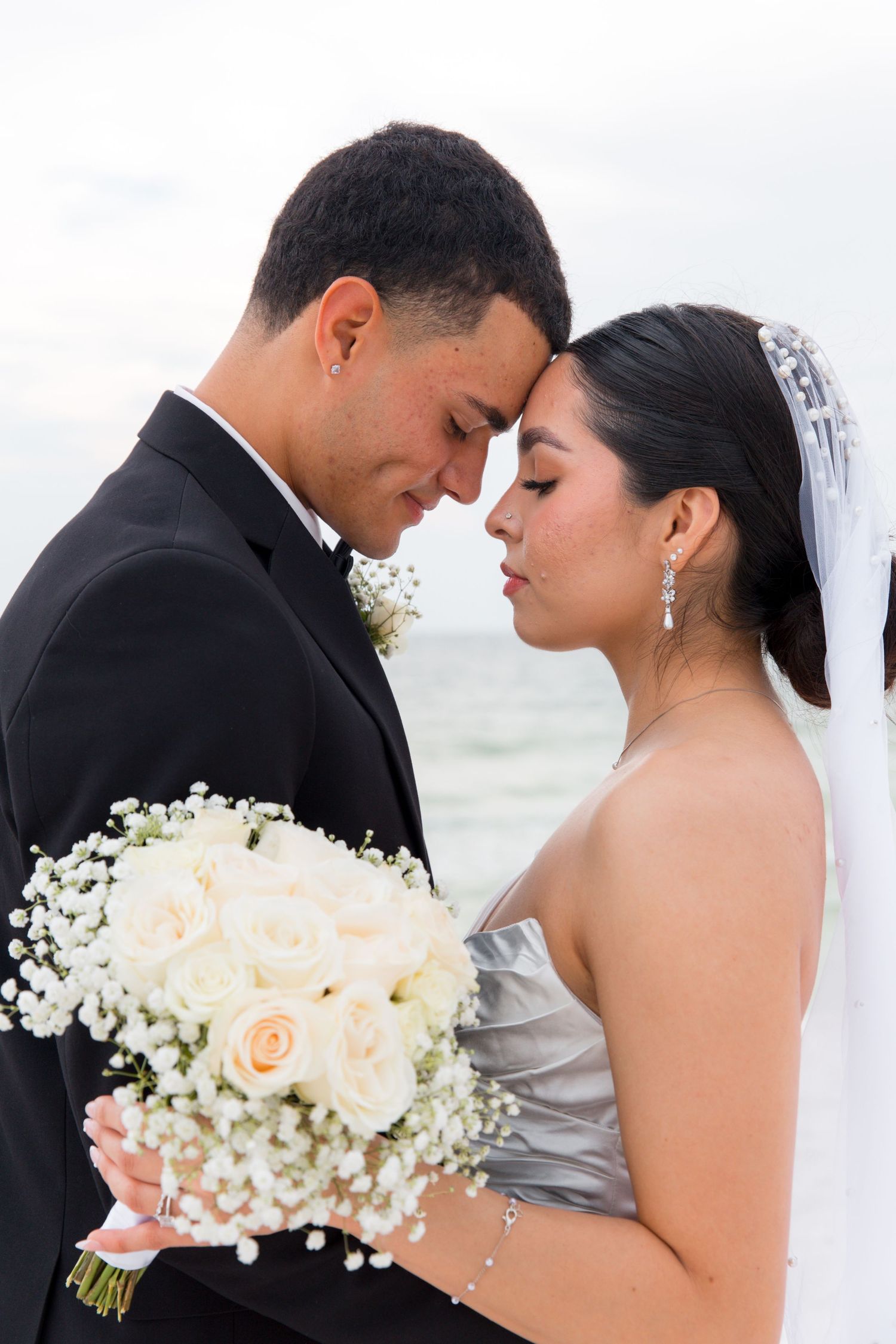Intimate moment between newlyweds with bride holding delicate rose and baby's breath bouquet.