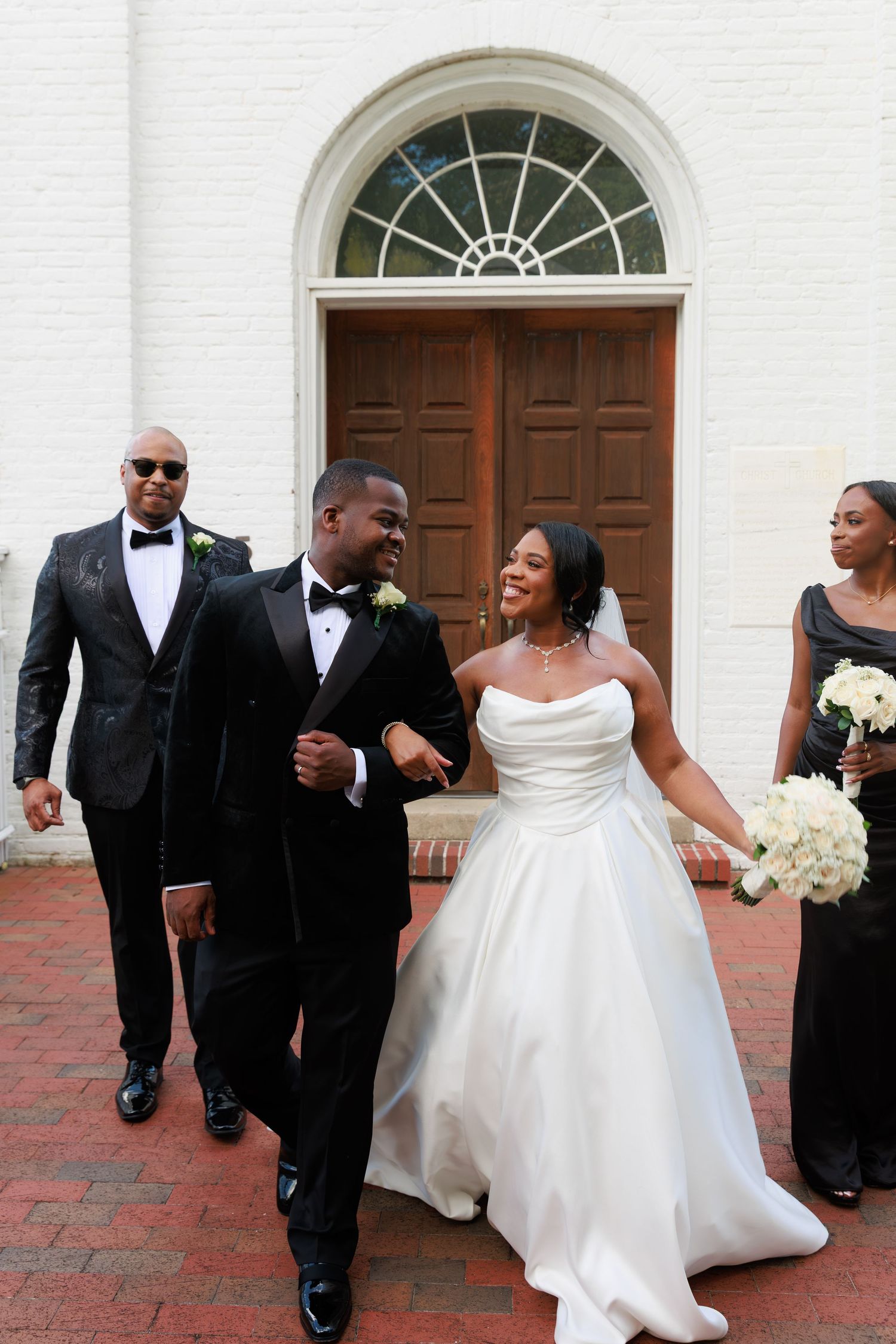 Wedding party members walk and celebrate together in front of a classic white church entrance.