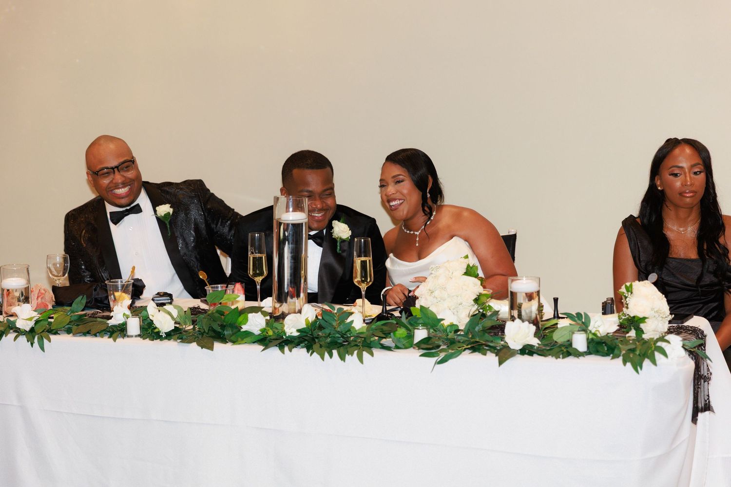 Long head table decorated with greenery garland and white linens at formal wedding reception.