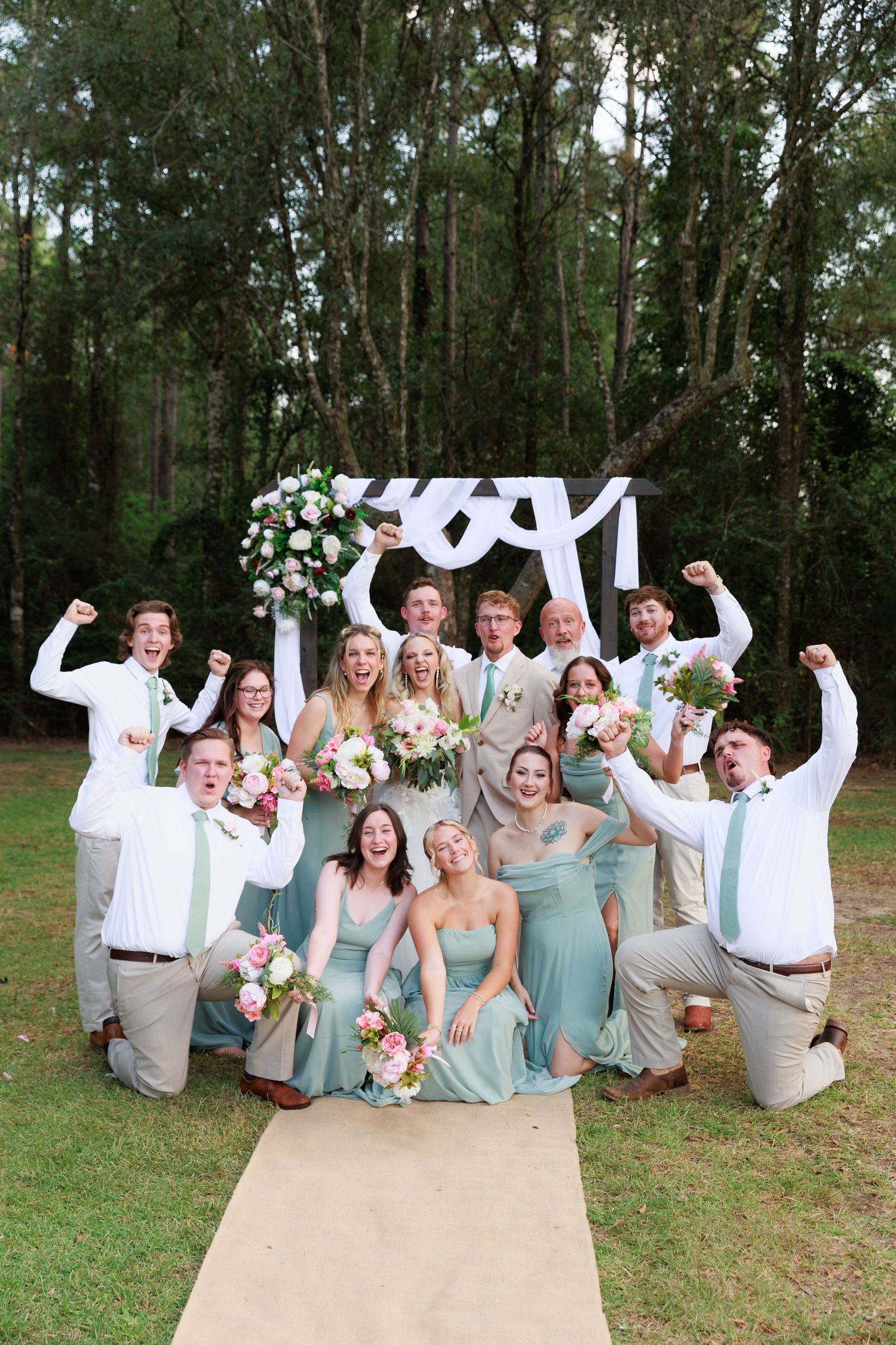 Wedding party members jump and celebrate on outdoor path while wearing coordinated mint green dresses and light suits.