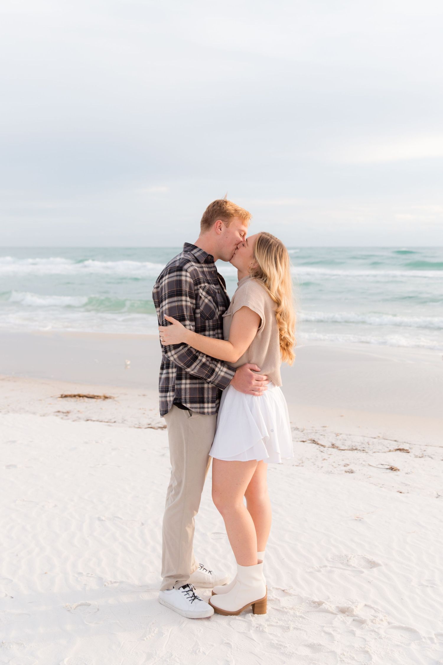 A romantic beach proposal scene with a couple embracing on pristine white sand by the ocean.