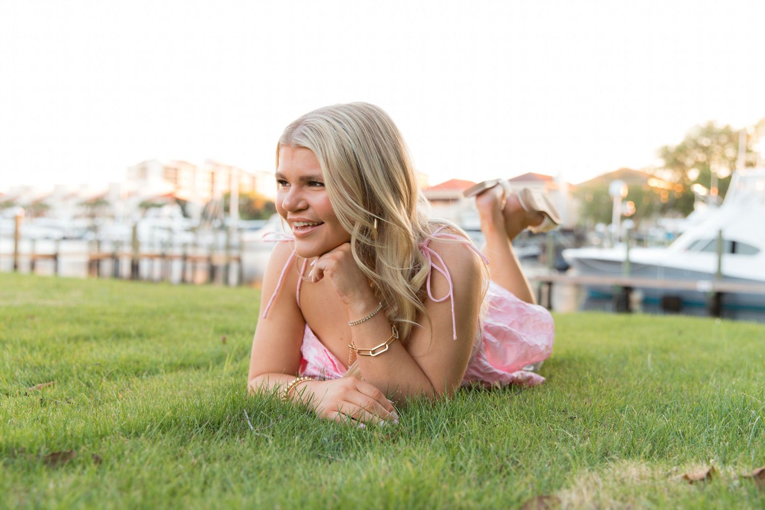 A person in a pink dress lies on green grass during golden hour sunset lighting.