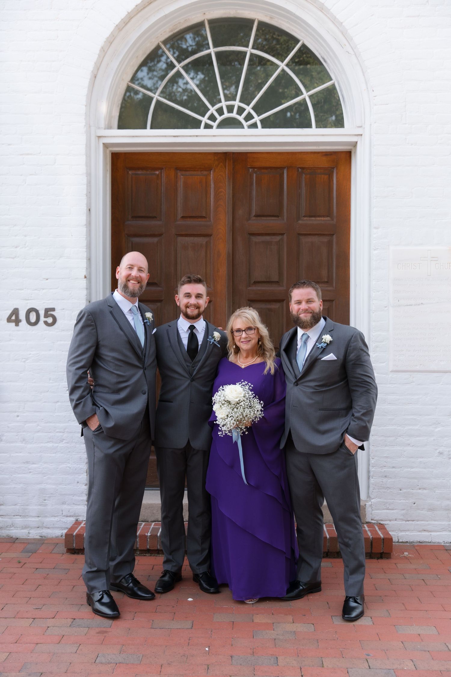 Four people posing in formal attire in front of historic church door with fanlight window.