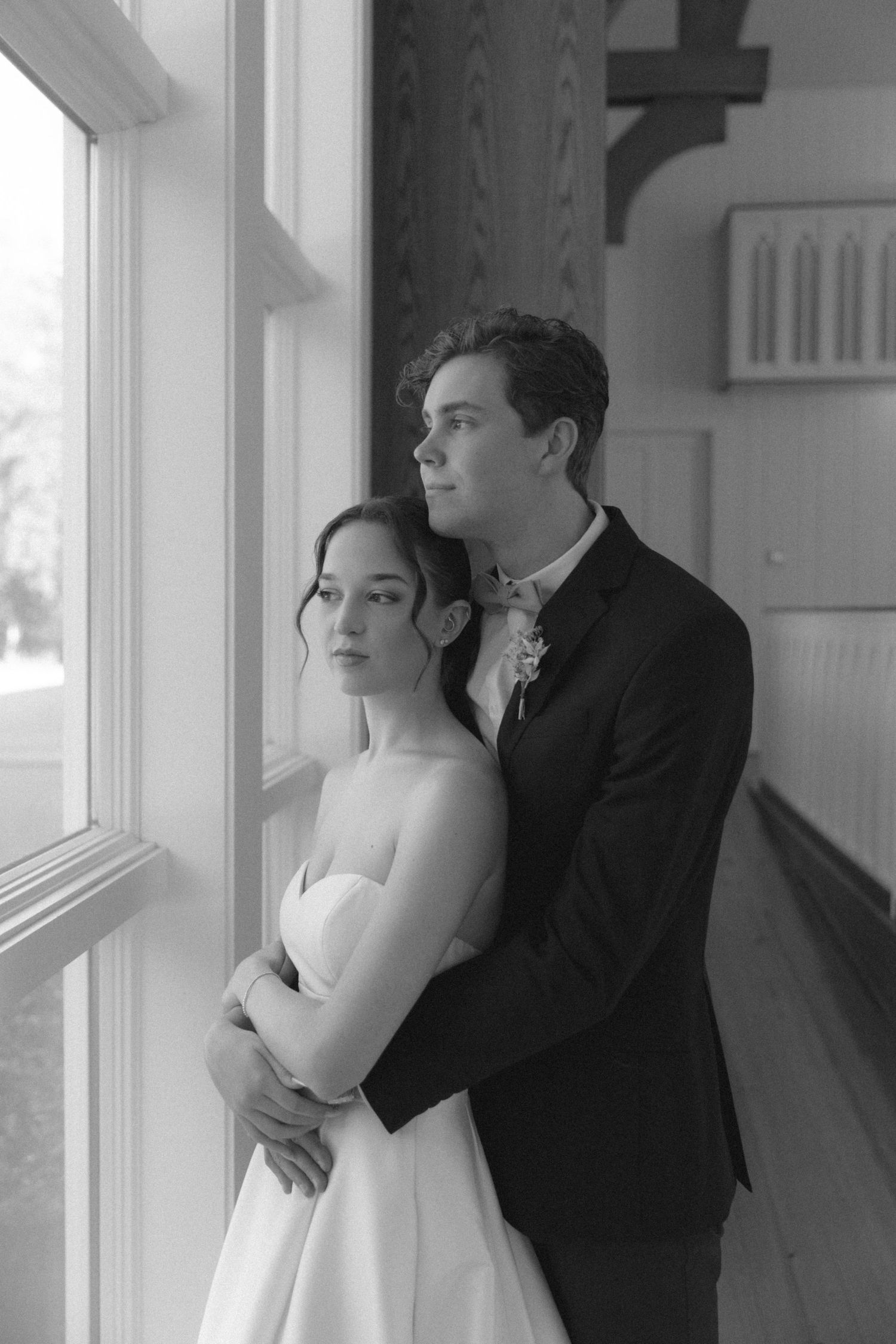 A black and white photo series showing a couple in formal attire embracing near large windows in an elegant interior space.