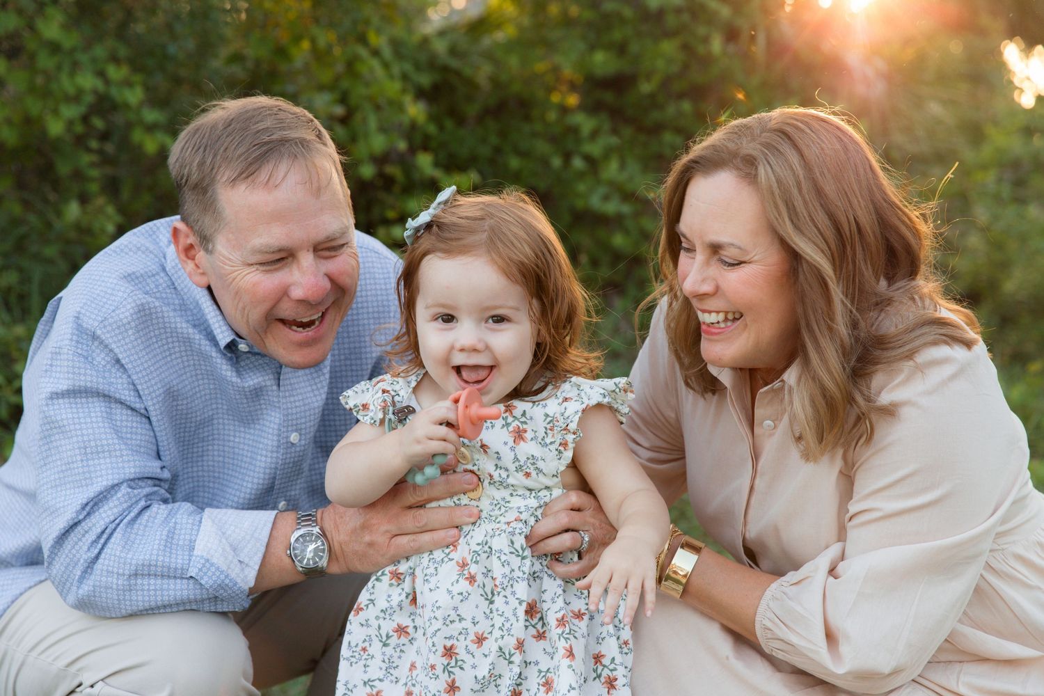 A joyful family moment captured during golden hour in a lush outdoor setting with warm sunlight filtering through trees.