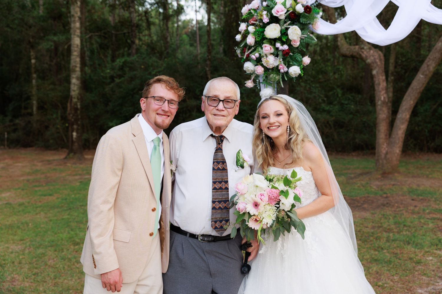 Wedding ceremony participants gather for group photos in a natural outdoor setting with trees.