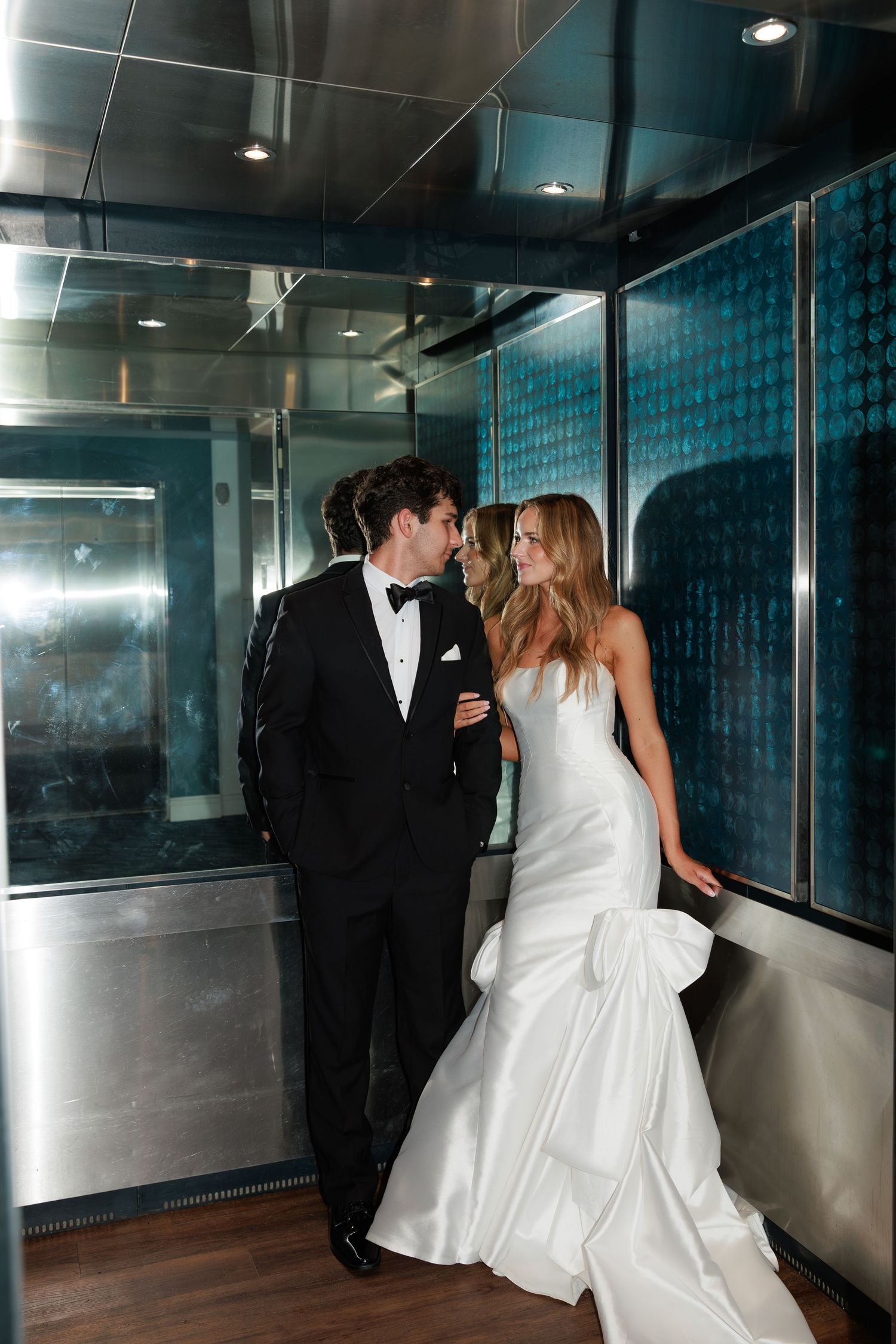 A couple in formal attire dances in an elegant modern hallway with blue-lit walls.