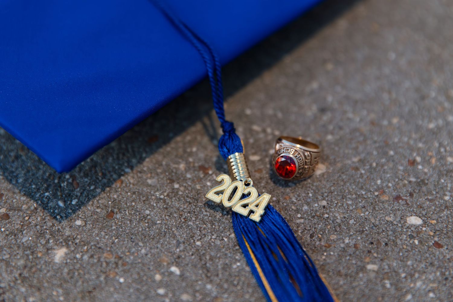 A 2024 graduation tassel and class ring with red stone rest beside a blue mortarboard cap.