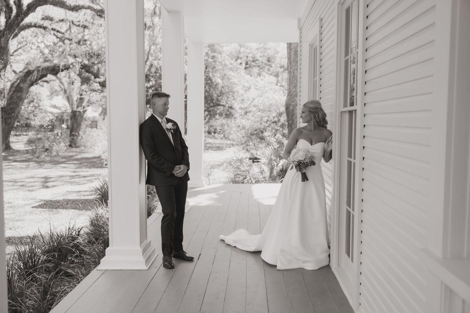 Black and white photo of bride and groom sharing first look moment on a classic white southern porch.