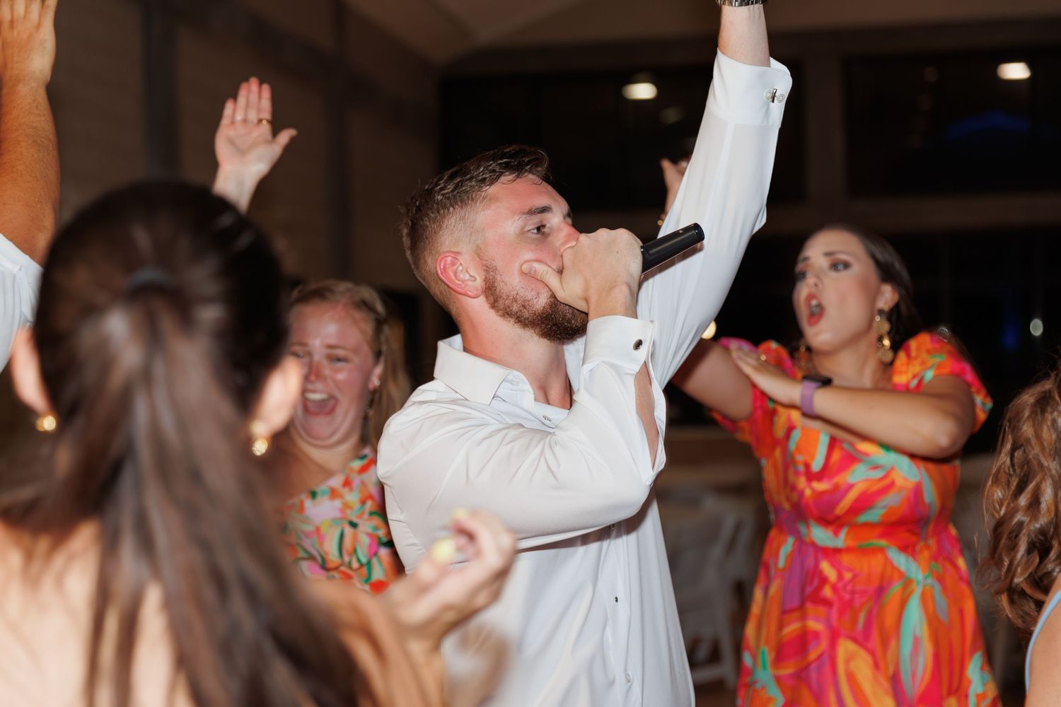 Wedding guests enthusiastically dancing and singing at a lively reception.
