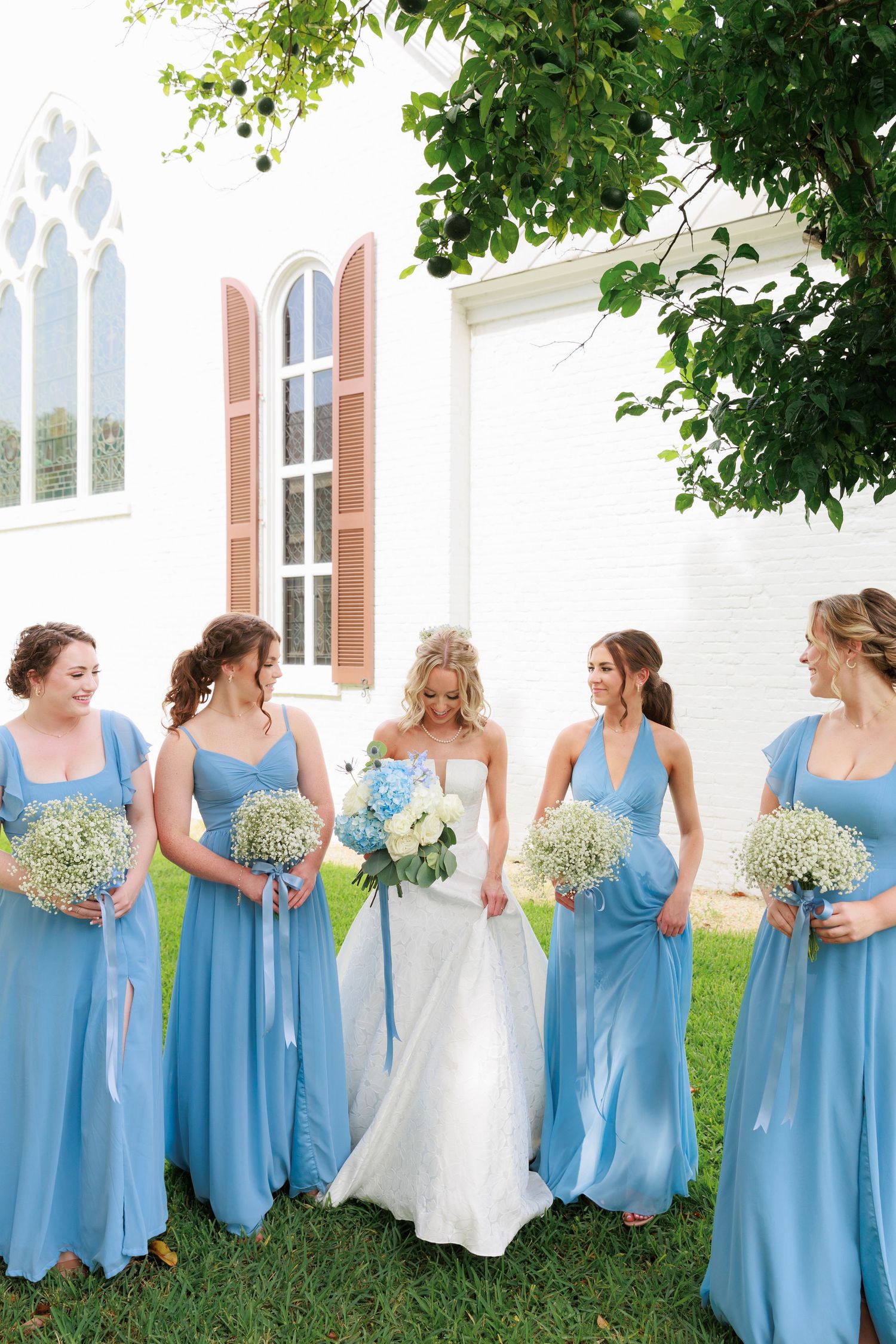 Bride in white gown stands with bridesmaids in light blue dresses holding white bouquets.