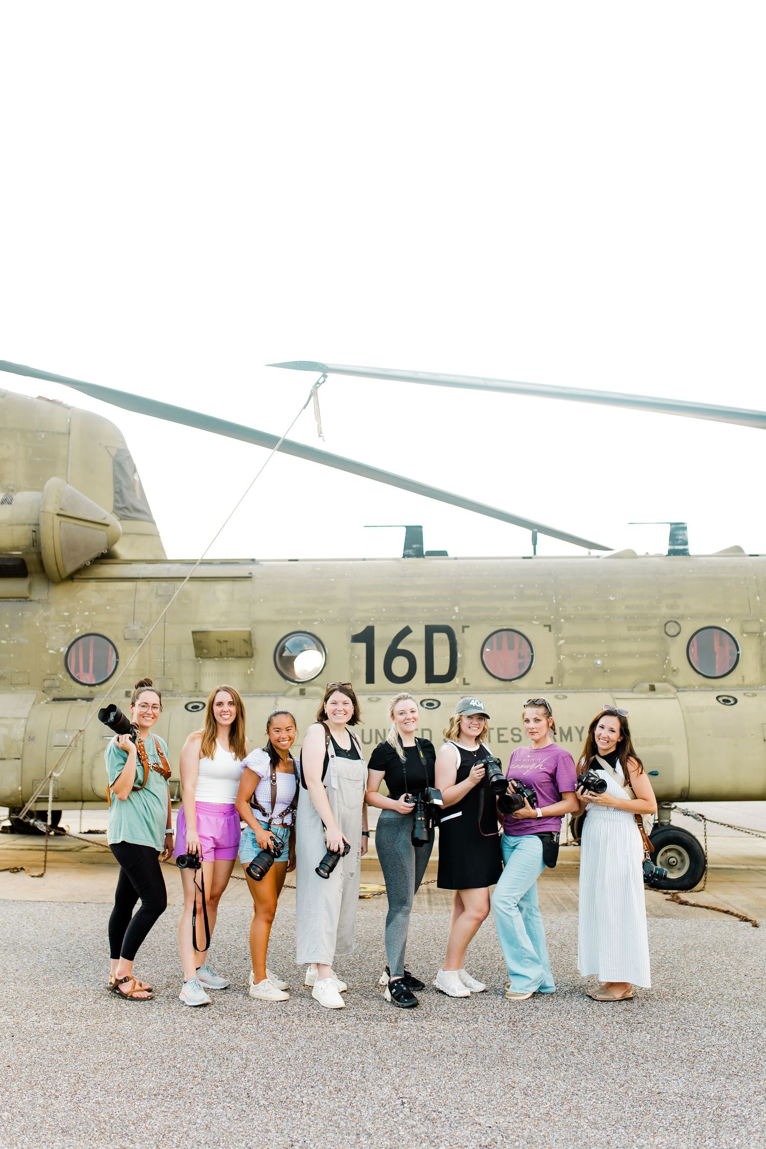 Group of women photographers posing together in front of a military helicopter.