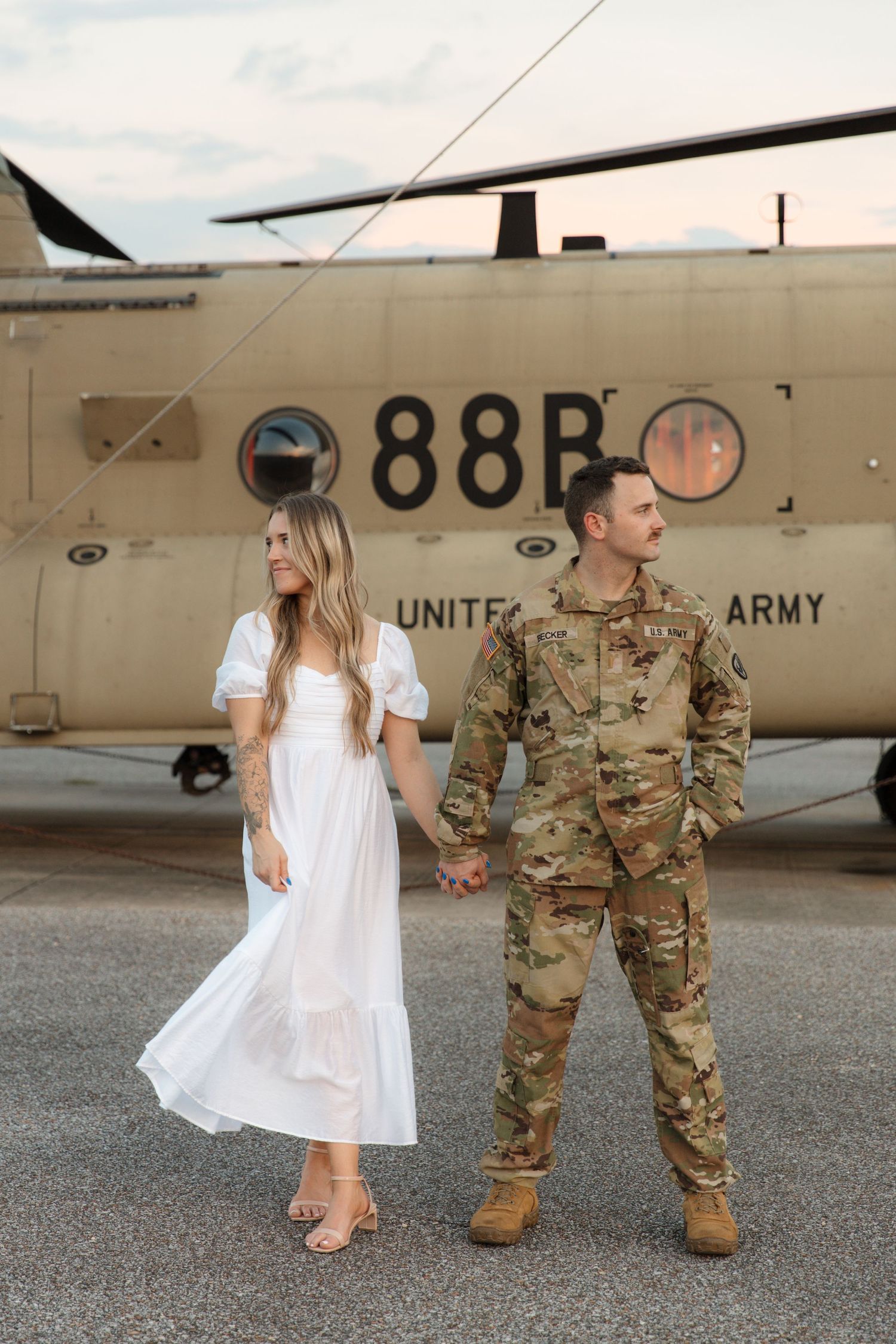 People walking near a US Army Chinook helicopter marked '88B' on a sunny tarmac.