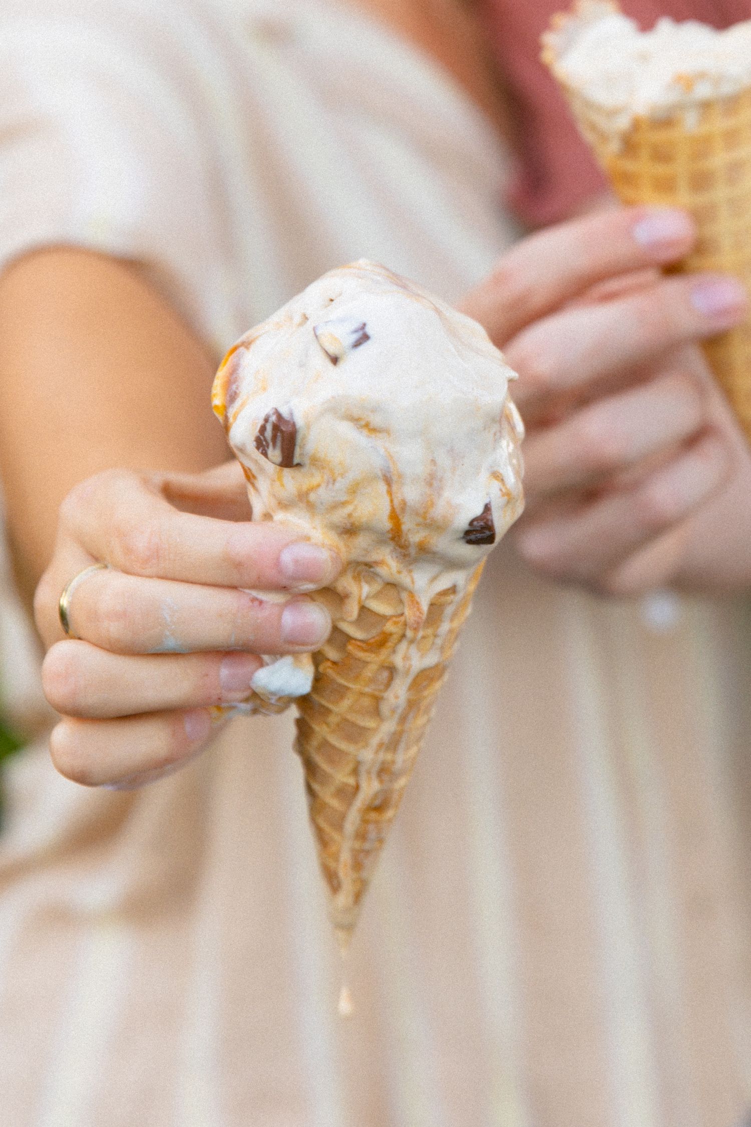 Close-up of a hand holding a melting vanilla and chocolate chip ice cream cone.